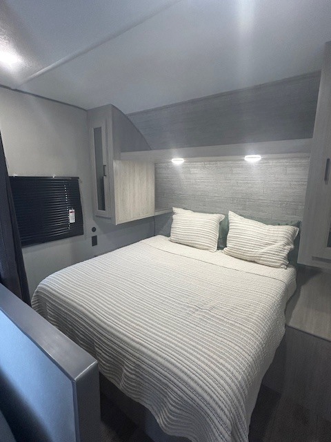 **RV rental** bedroom features a cozy, striped bed, textured headboard, and bright reading lights.. Coachman RV 261BH 2025