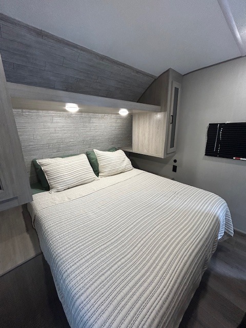 Modern rv rental bedroom: a cozy bed with white striped comforter, light grey headboard, and built-in storage.. Coachman RV 261BH 2025