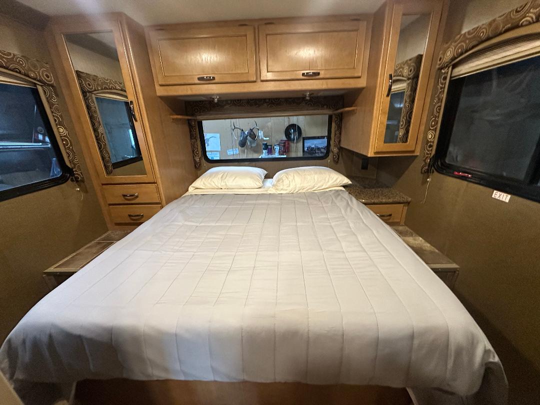 Inside this RV rental bedroom: a comfortable bed, wood cabinets, mirrors, and windows. Perfect for road trips.. Thor Four Winds 2016