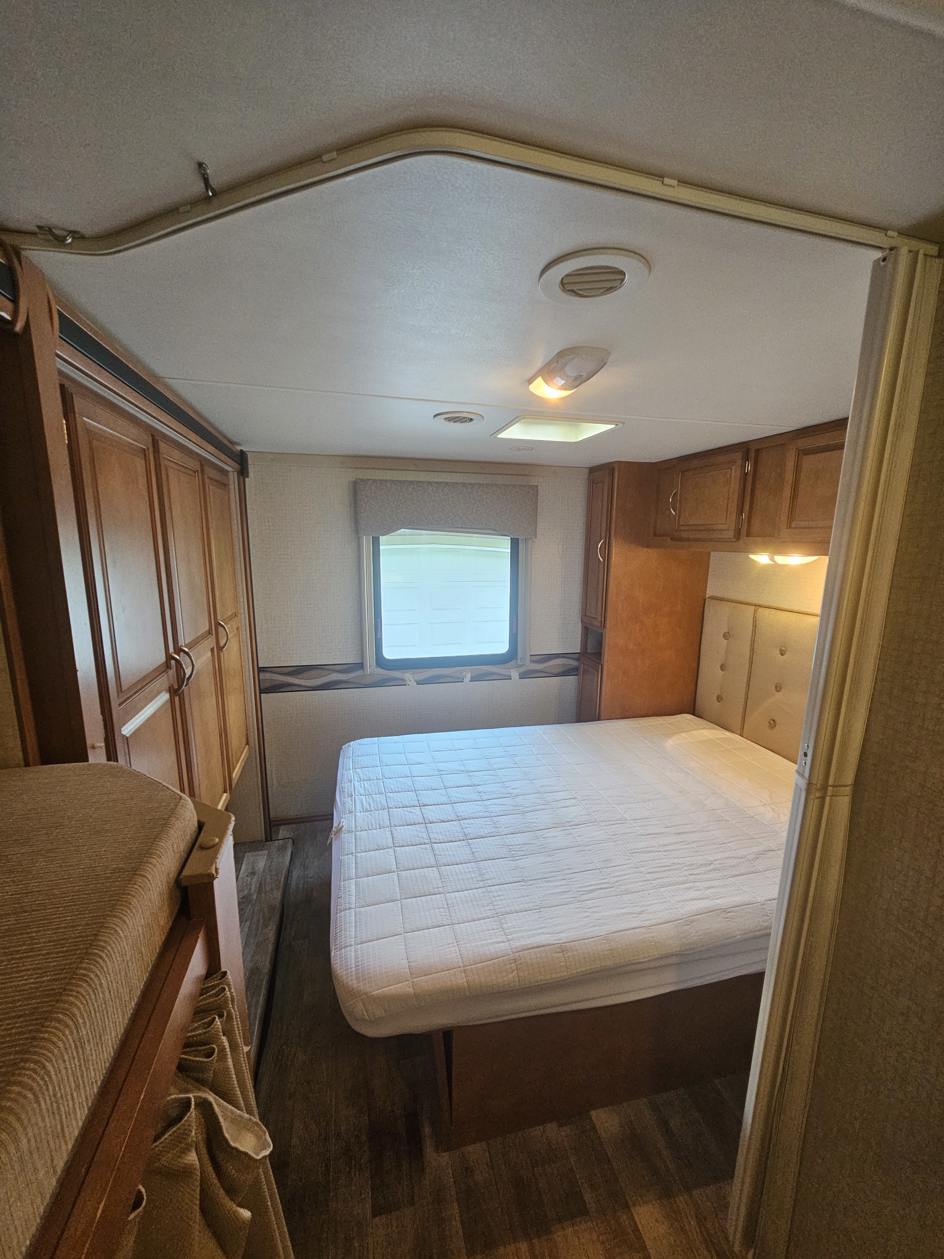 Inside an RV rental: a compact bedroom featuring a bed with a quilted mattress, wooden cabinetry, and a bunk bed.. Other Other 2017