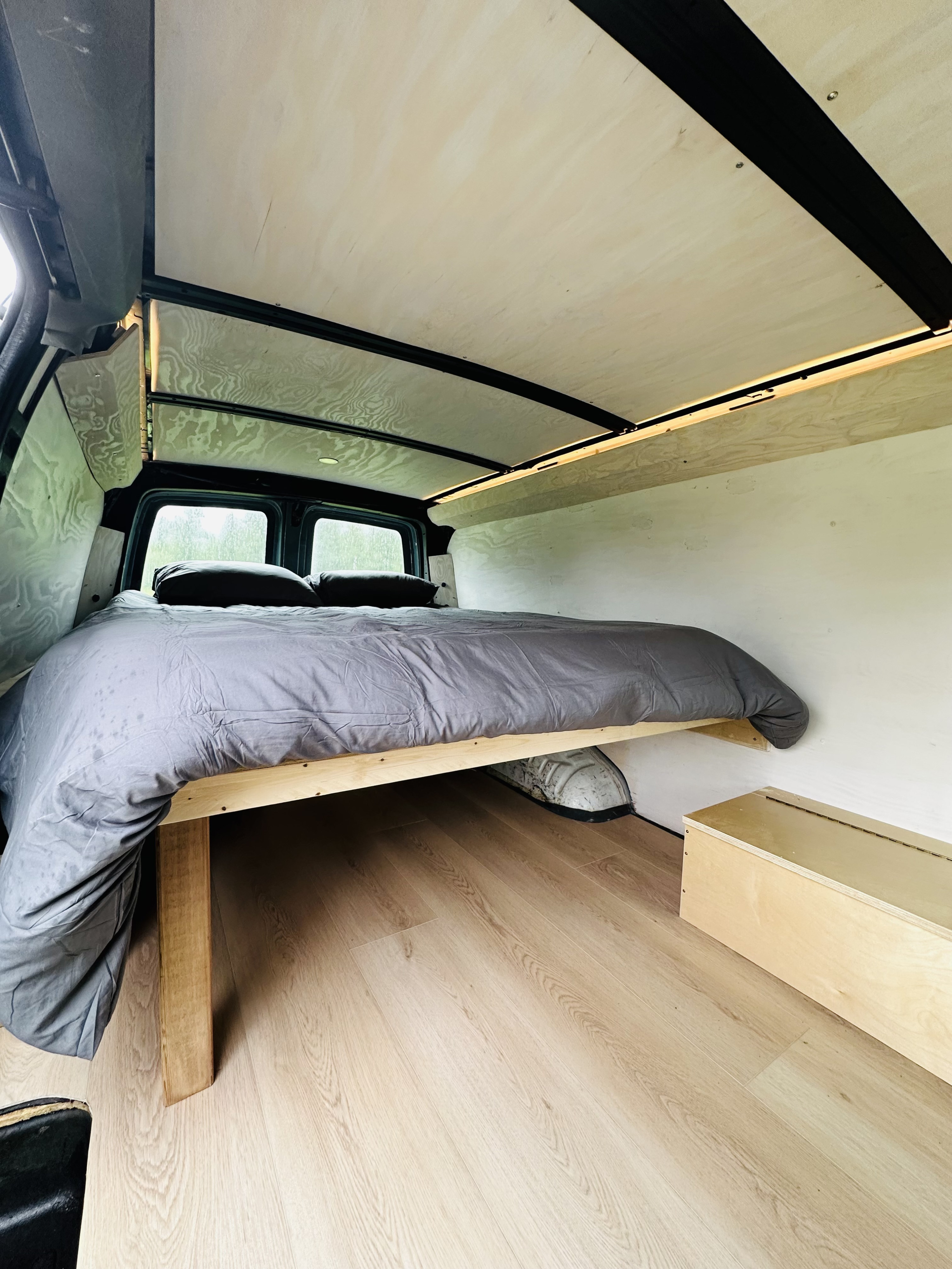 Inside a modern RV rental: custom bed, light wood interior, and ambient lighting create a cozy camper van retreat.. Chevrolet Express 2003