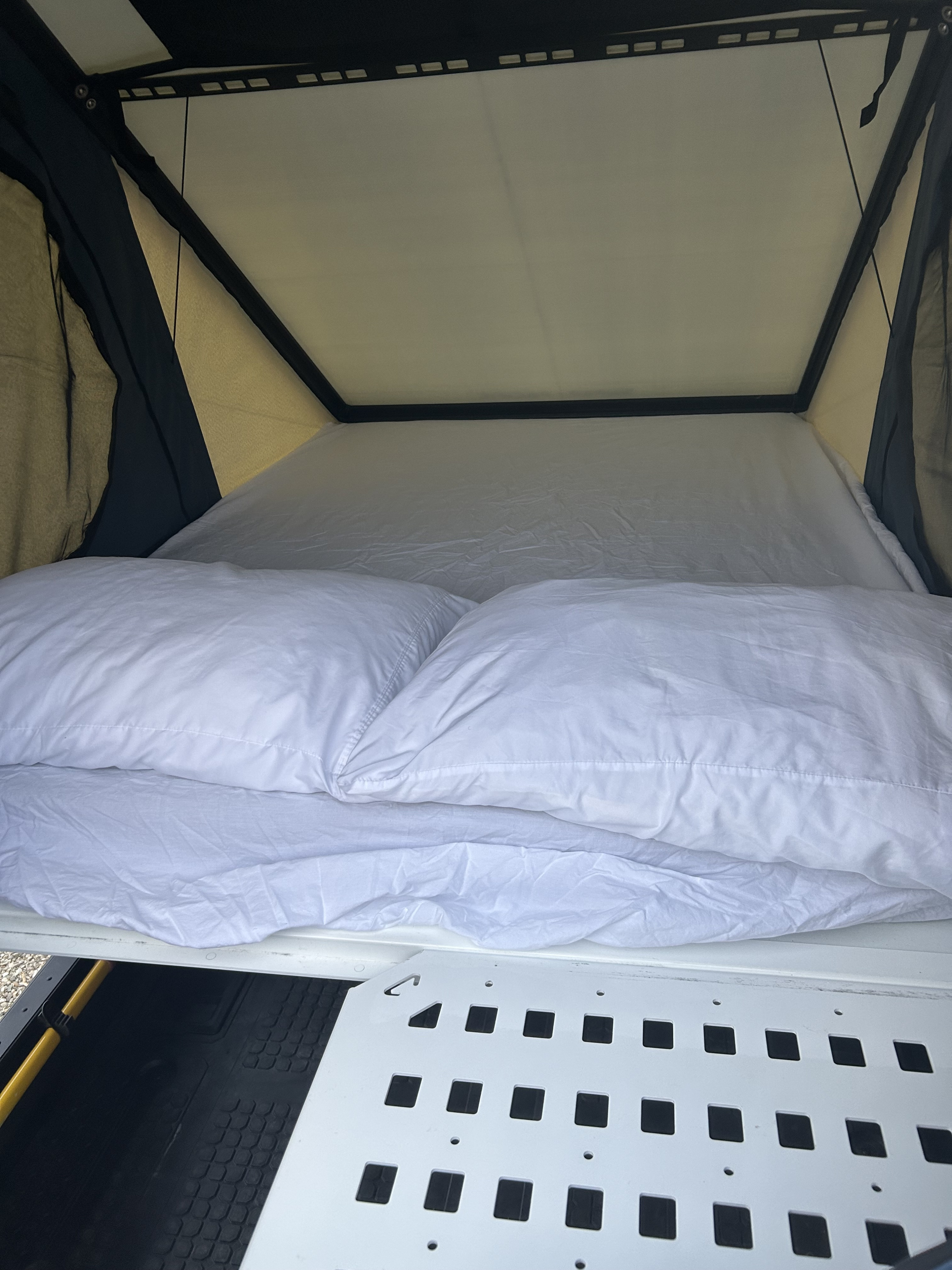 Cozy white bedding and pillows inside a pop-up RV rental rooftop tent, ready for a comfortable night.. Dodge Dodge 1 Ton Pu 2018