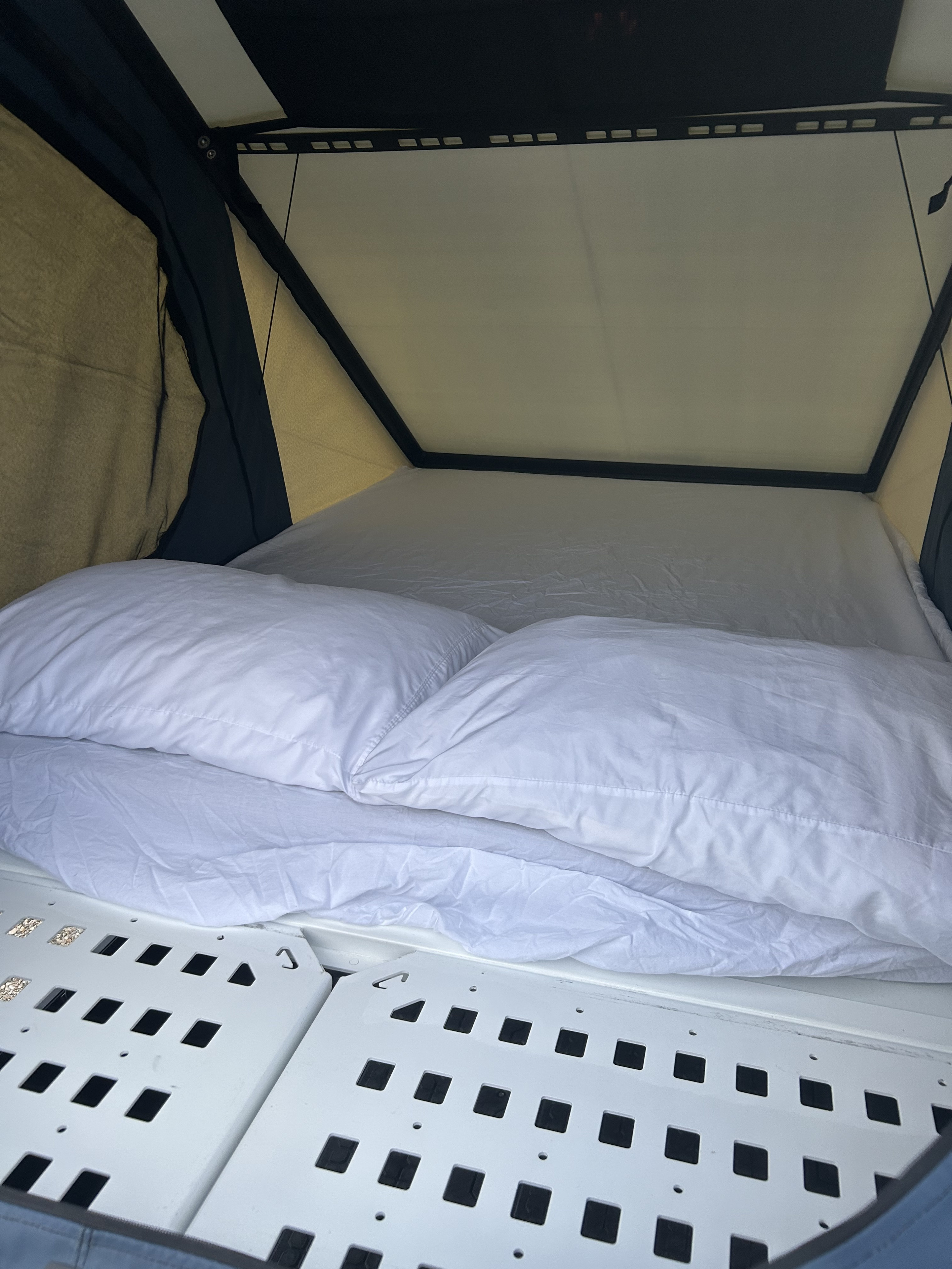 Cozy RV rental interior showing a neat bed with white pillows and sheets inside a pop-up tent with a perforated base.. Dodge Dodge 1 Ton Pu 2018