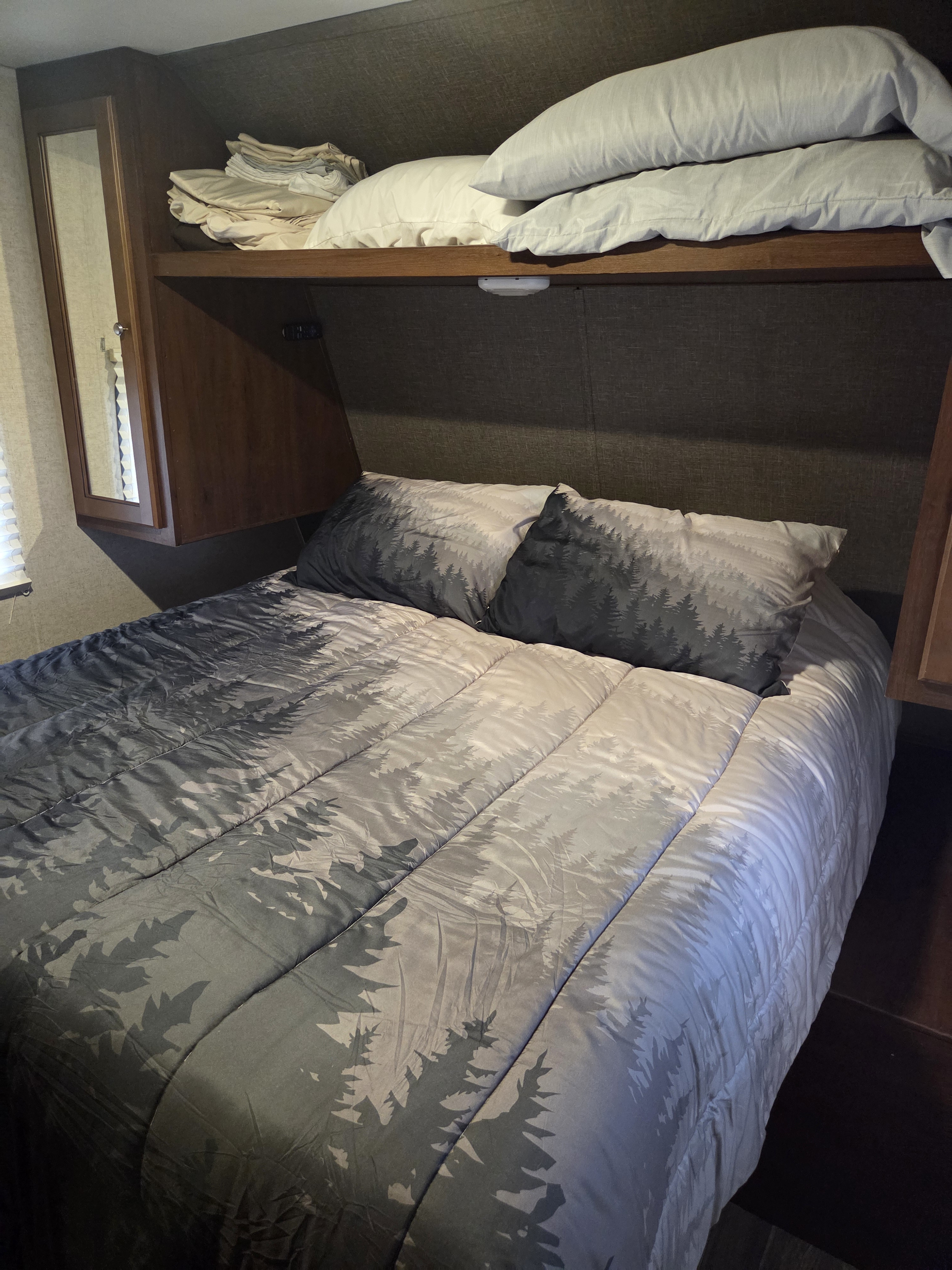 RV rental bedroom with comfortable tree-patterned bedding and pillows, plus built-in overhead storage for your journey.. Heartland RVs Trail Runner SLE 2017
