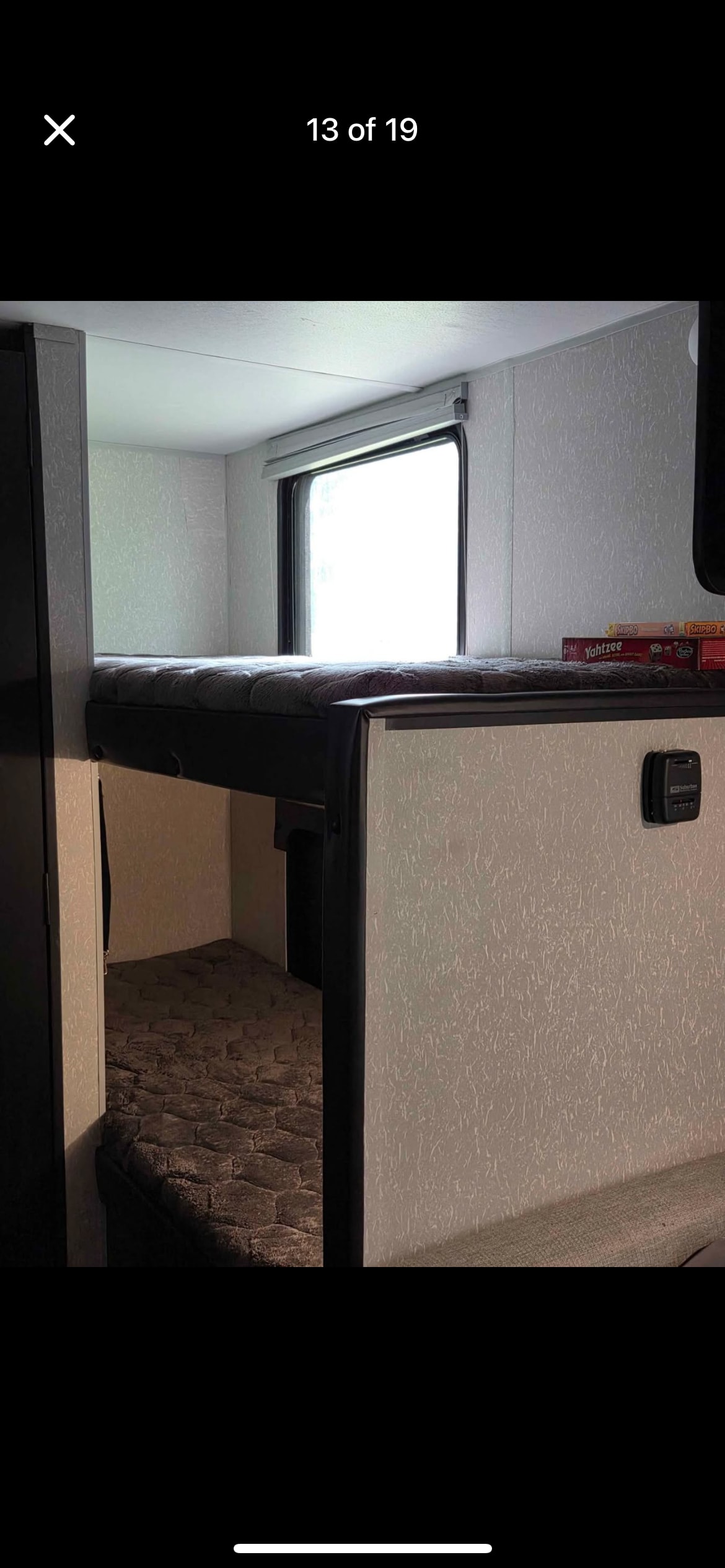 RV rental interior featuring cozy bunk beds. The top bunk has a window and a stack of board games, with the lower bunk visible below.. Forest River Cherokee Wolf Pup Black Label 2022