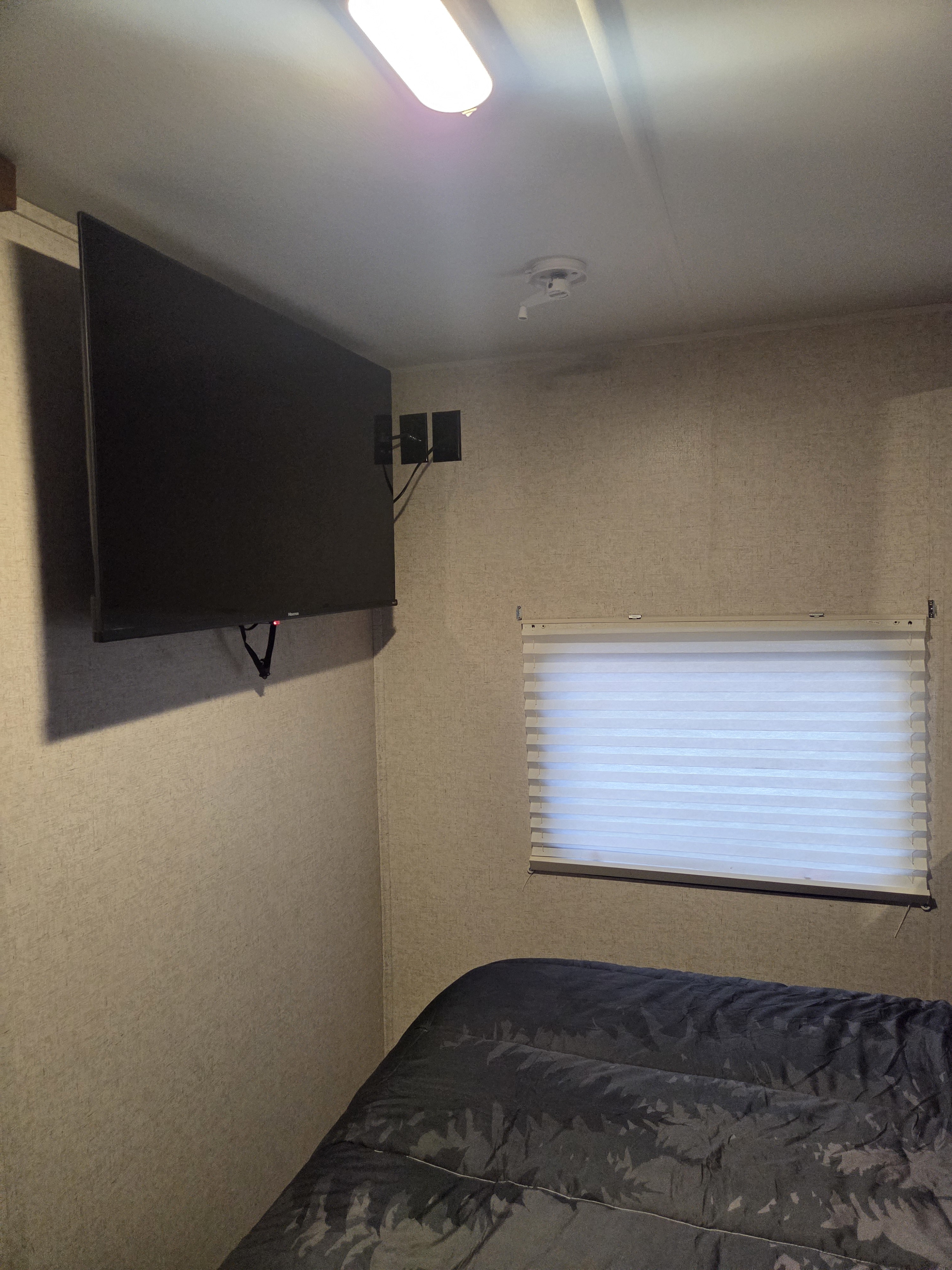 Inside an RV rental: A bedroom with a mounted TV, window with blinds, and a dark comforter on the bed.. Heartland RVs Trail Runner SLE 2017