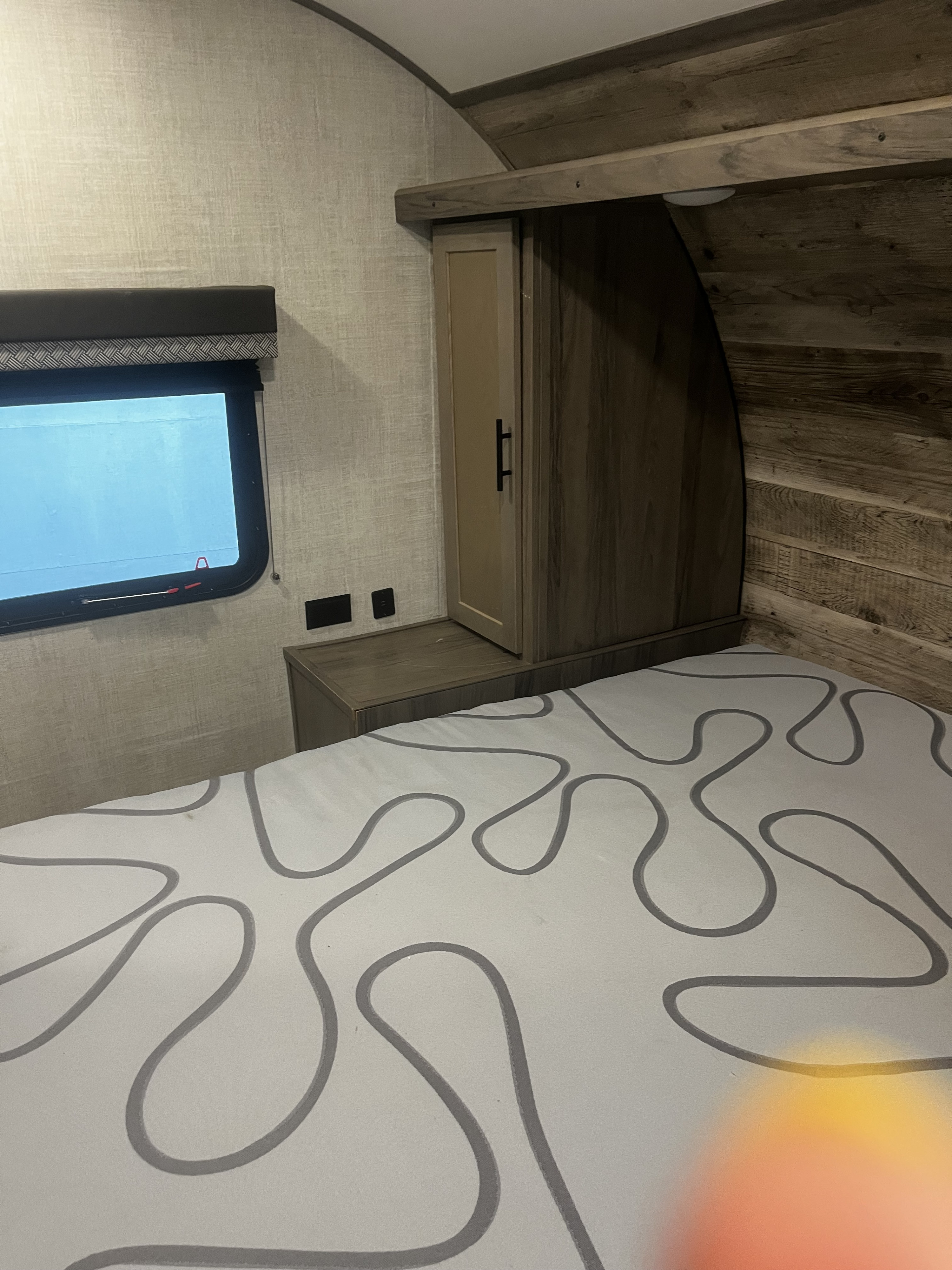 Modern RV rental bedroom interior with patterned bed, window, and wood-toned built-in cabinet for comfortable travel.. Gulf Stream Innsbruck 2022
