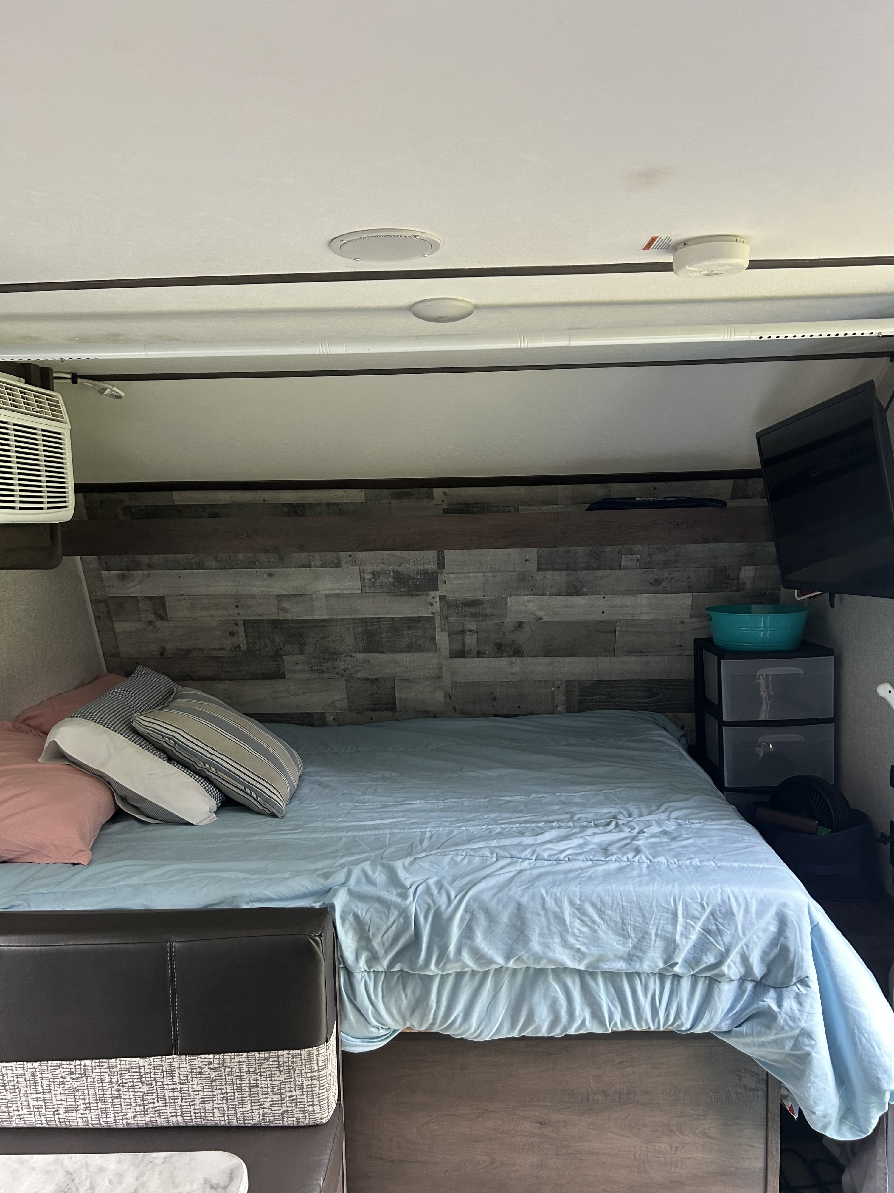 RV rental bedroom: light blue bed, wood accent wall, wall-mounted TV, and compact storage. Practical, cozy interior.. Dutchmen Coleman Lantern LT 2021