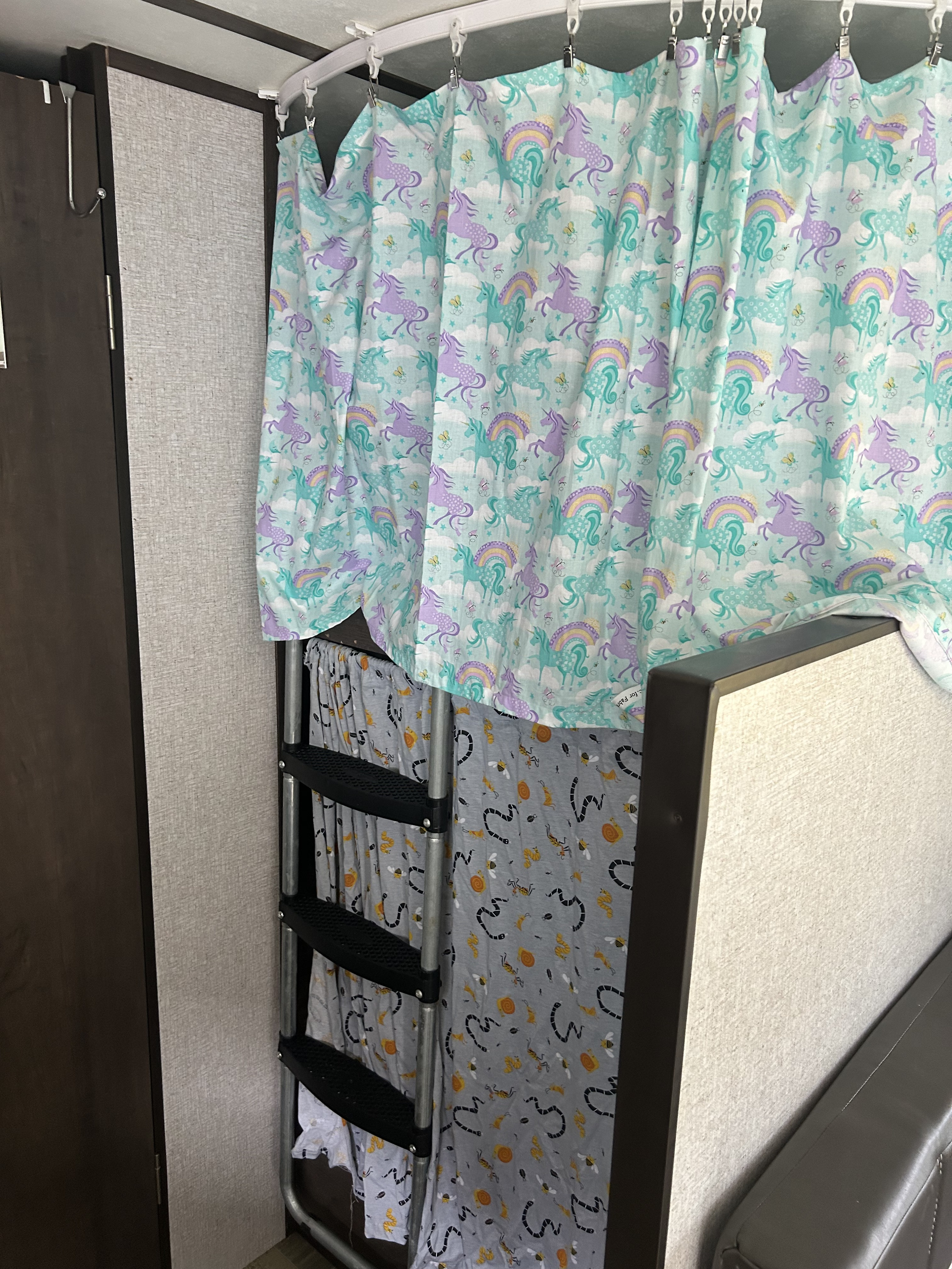 Colorful privacy curtains on bunk beds in an RV rental, featuring unicorn and insect patterns with a ladder.. Dutchmen Coleman Lantern LT 2021
