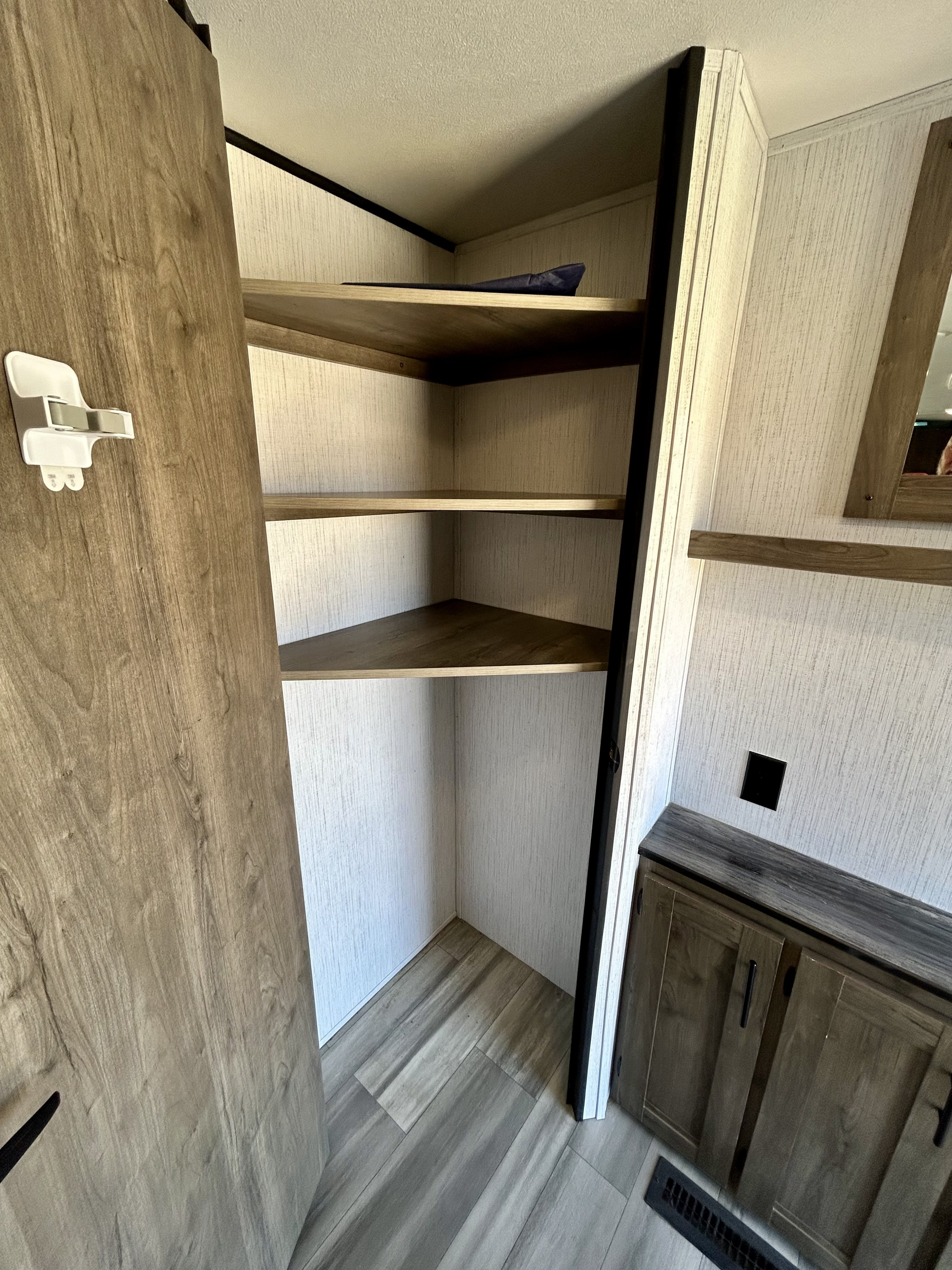 RV rental interior: corner shelves, an open closet, cabinet, light walls, and wood-look floor.. Heartland RVs Pioneer 2022