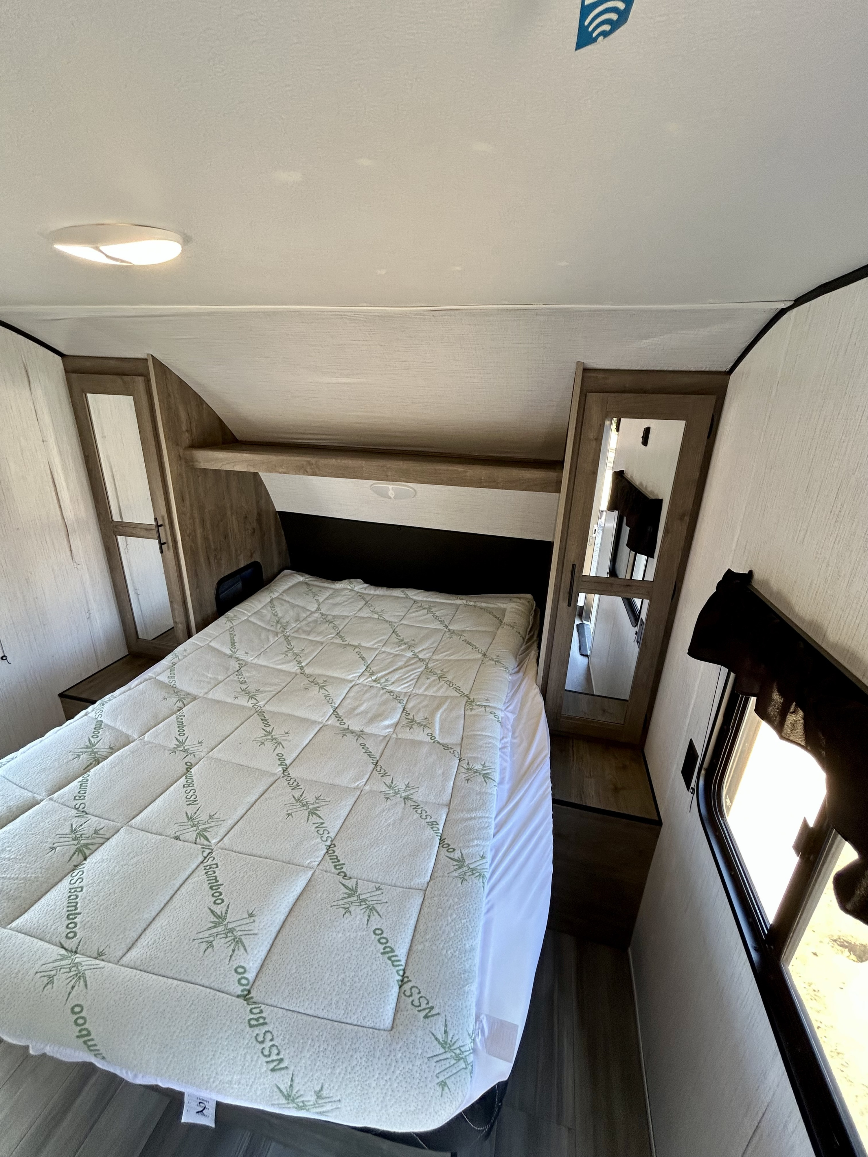 This RV rental bedroom features a comfortable bed with an "NSS Bamboo" mattress topper, built-in storage, and natural light from a window.. Heartland RVs Pioneer 2022