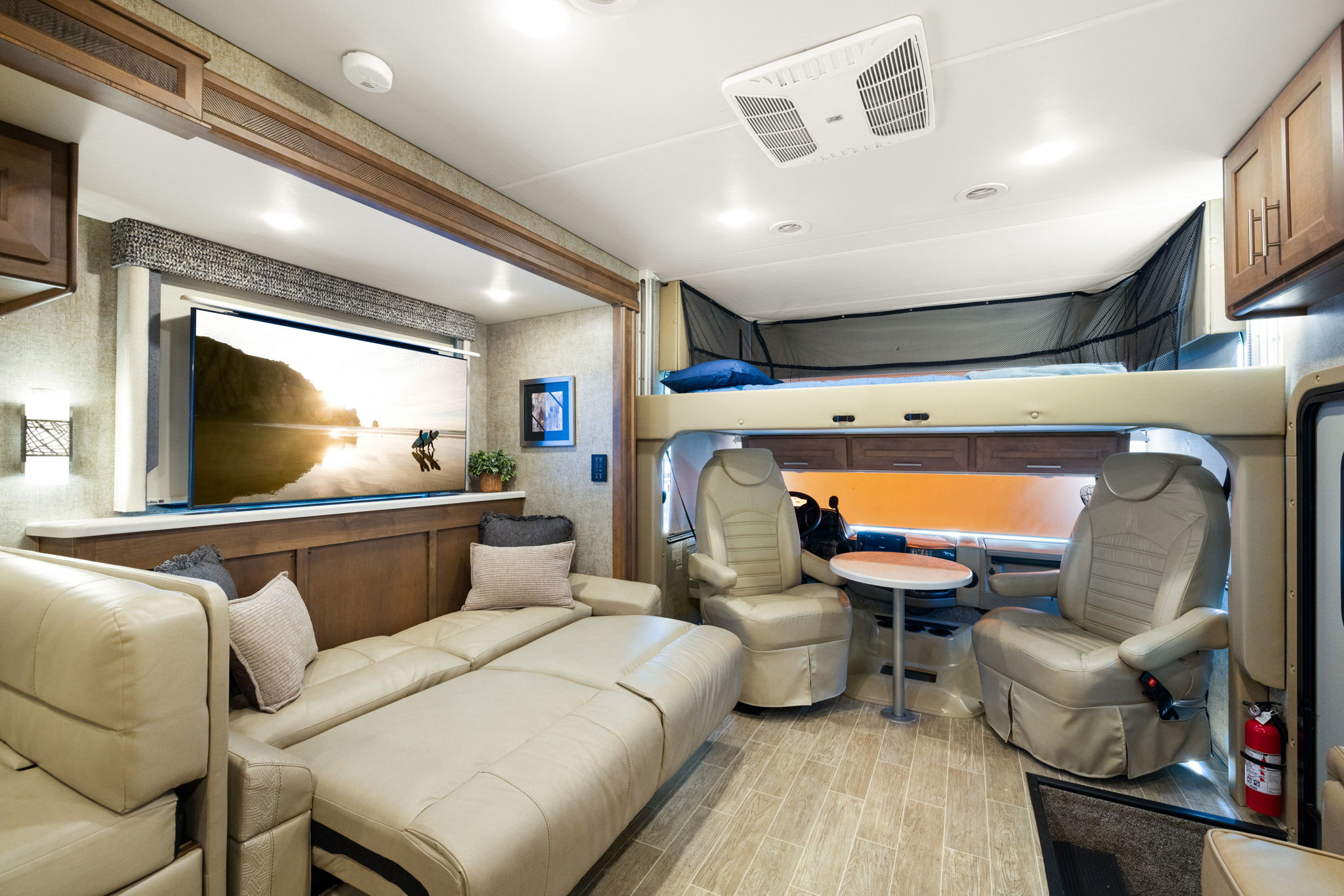 Modern RV rental interior showing living area with sofa, TV, overhead bunk bed, swivel captain's chairs, and dining table.. Thor Miramar 2021
