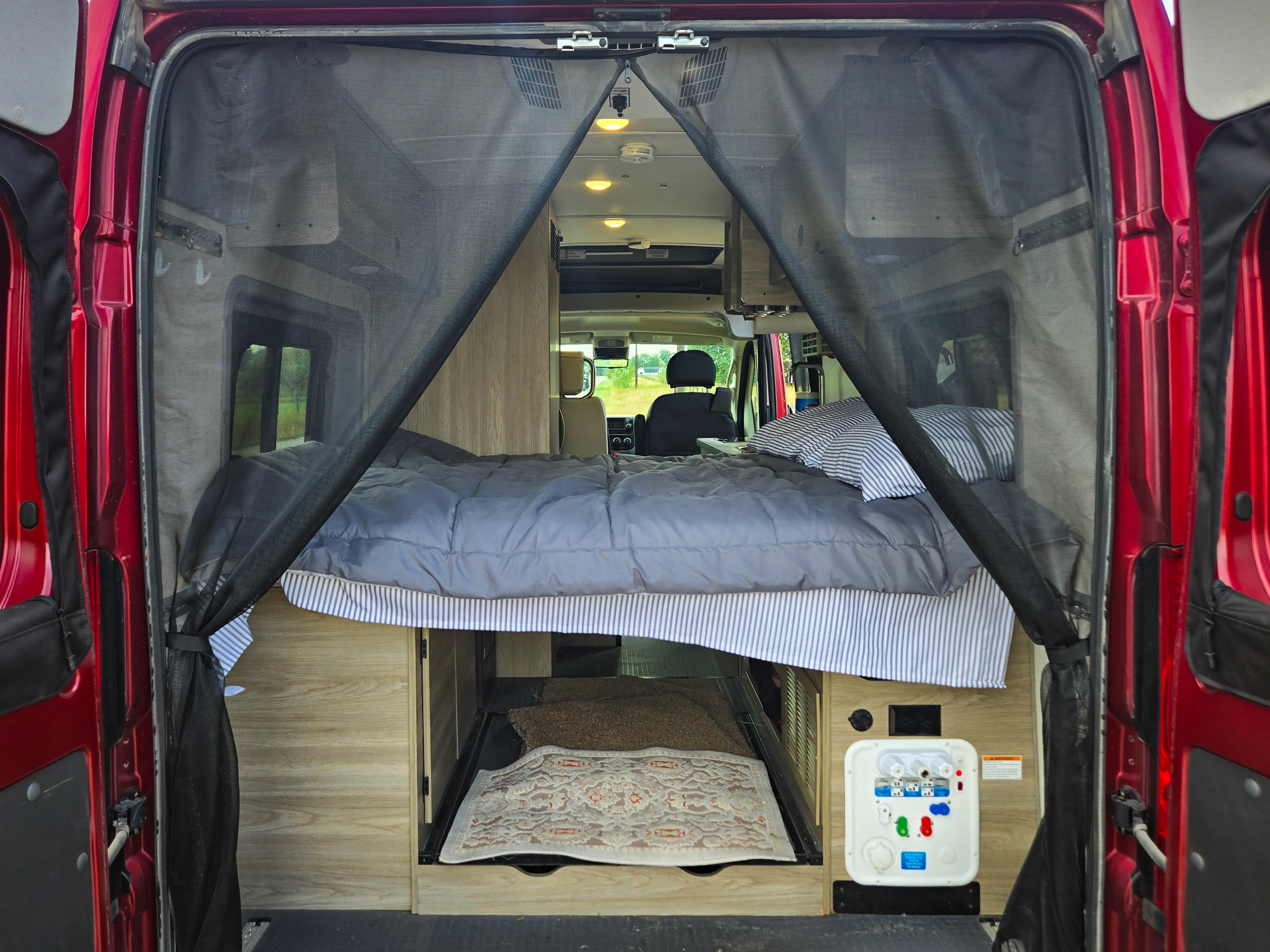 Inside a comfy RV rental: bed, under-bed storage, and utility panel, with a protective bug screen at the rear.. Winnebago Solis 2021