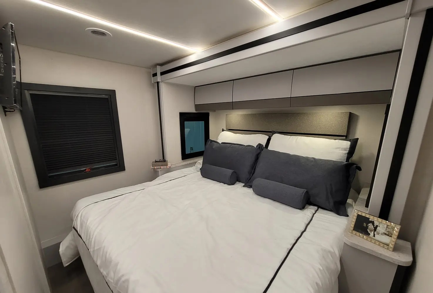 Modern RV rental bedroom with queen bed, white and gray bedding, overhead storage, ambient lighting, and side windows.. Coachmen Euro 2025