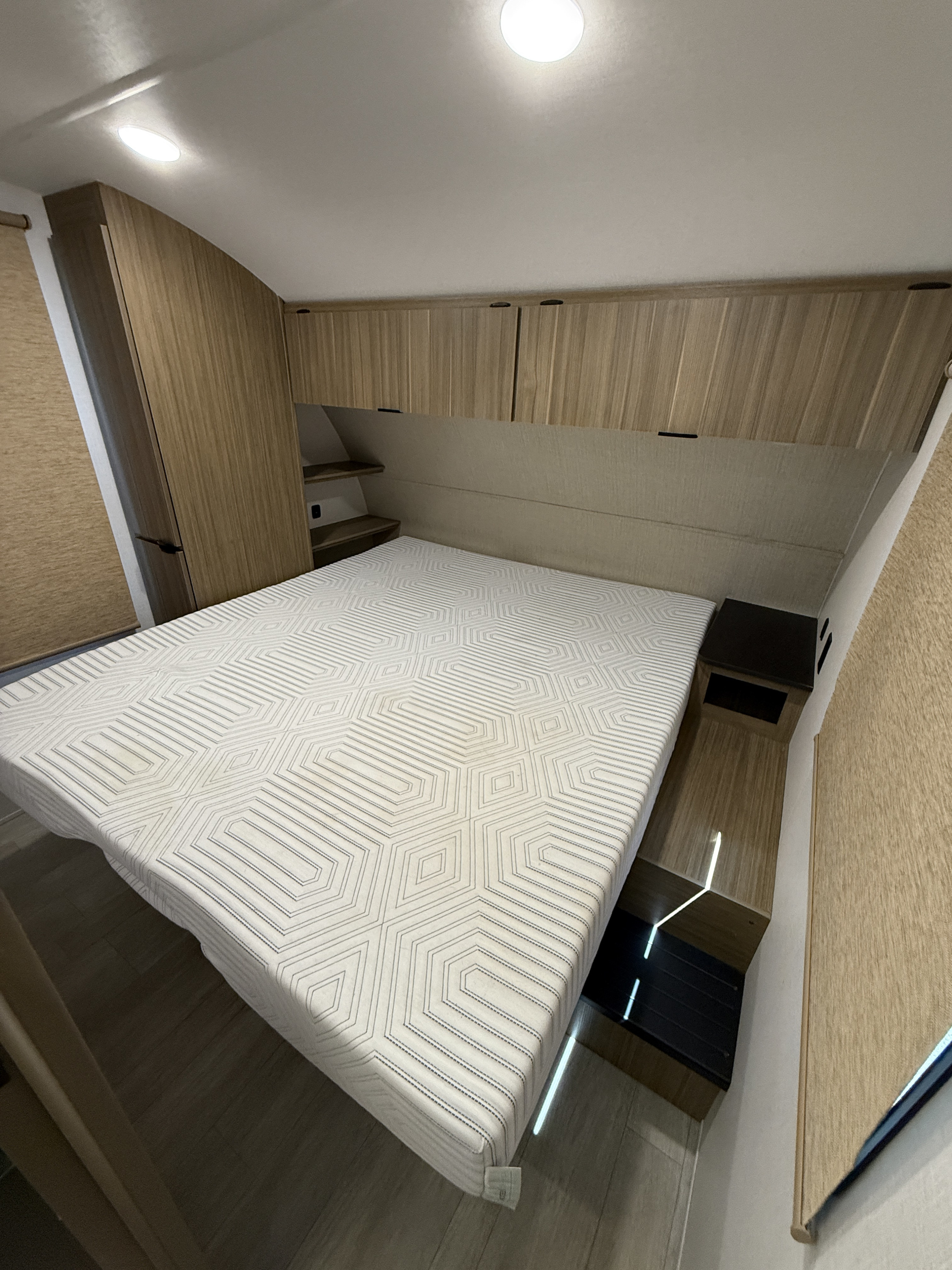 Modern RV rental bedroom features a bed with geometric mattress, light wood cabinets, and integrated storage solutions.. Forest River 273QBXL 2024