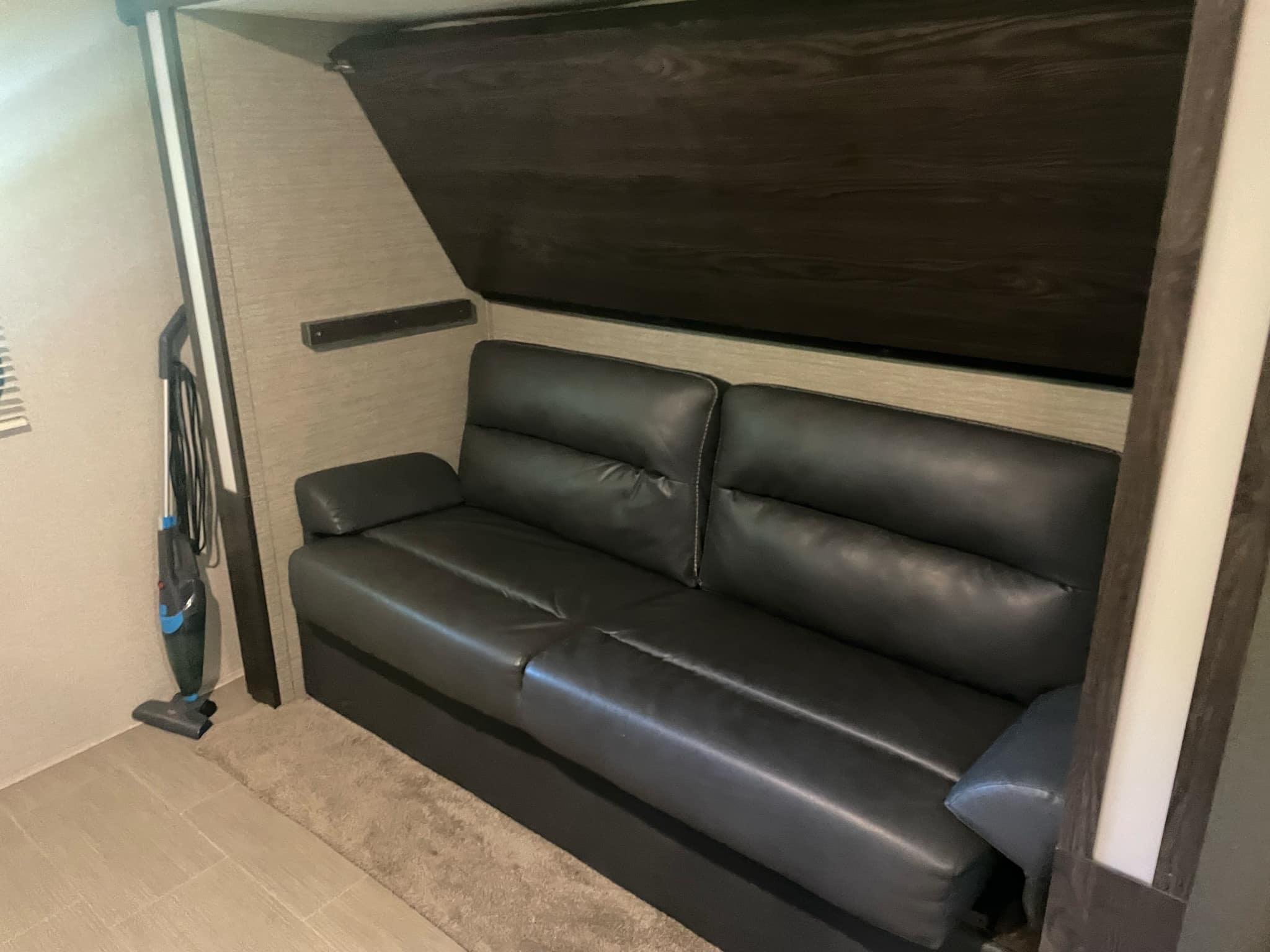Inside an RV rental: a comfortable black sofa, with a compact vacuum for easy cleanups in this living space.. Dutchmen Kodiak Ultra-Light 2018