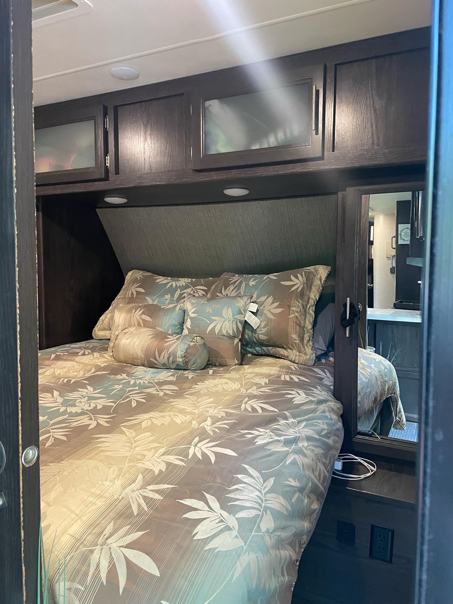 Inside an RV rental: a compact bedroom with patterned bed, overhead cabinets, and side mirror. Your travel retreat.. Dutchmen Kodiak Ultra-Light 2018
