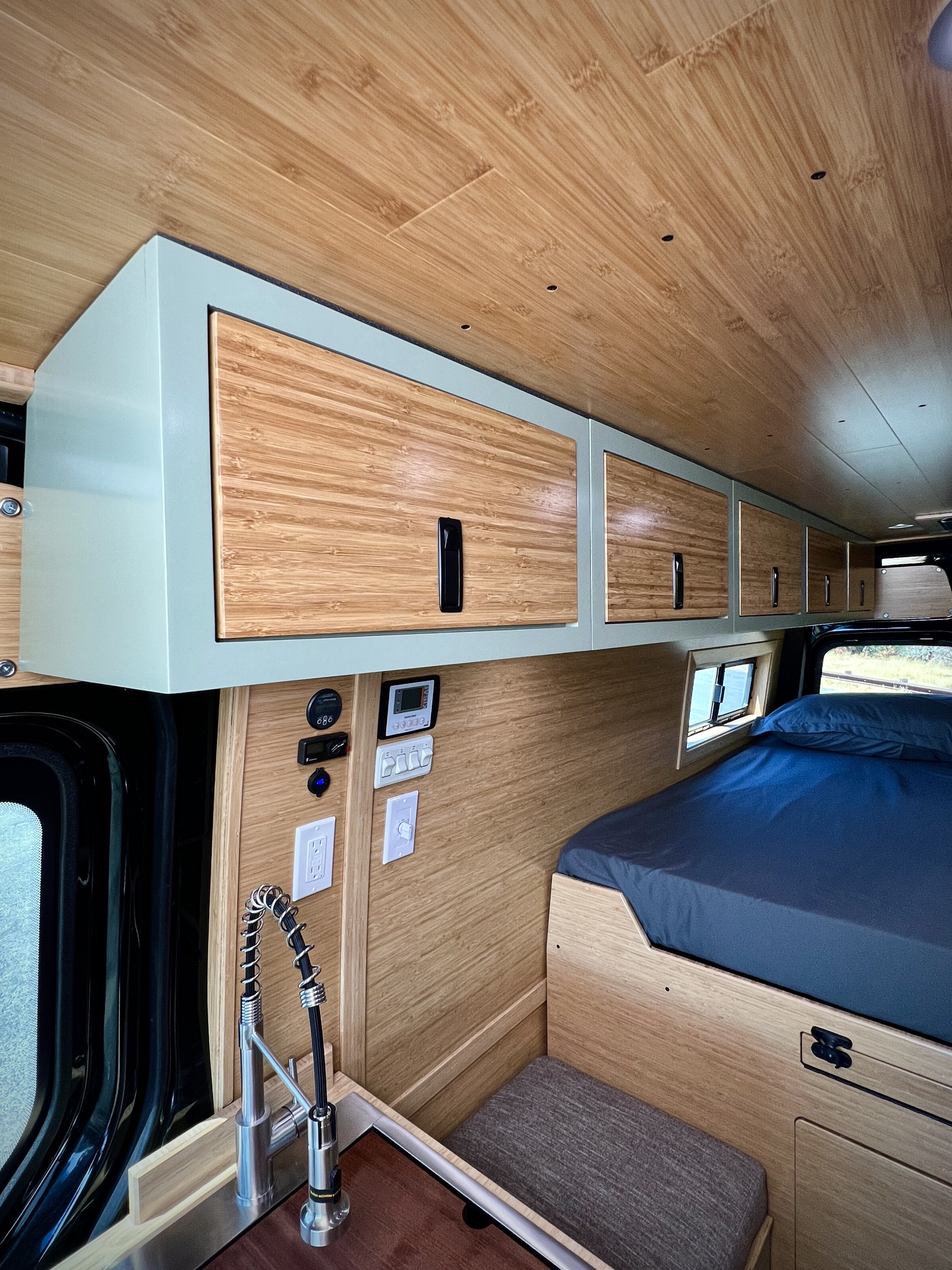 Modern RV rental interior with bamboo walls, overhead mint cabinets, kitchen sink, and bed on the right.. Mercedes-Benz Sprinter 2500 2024
