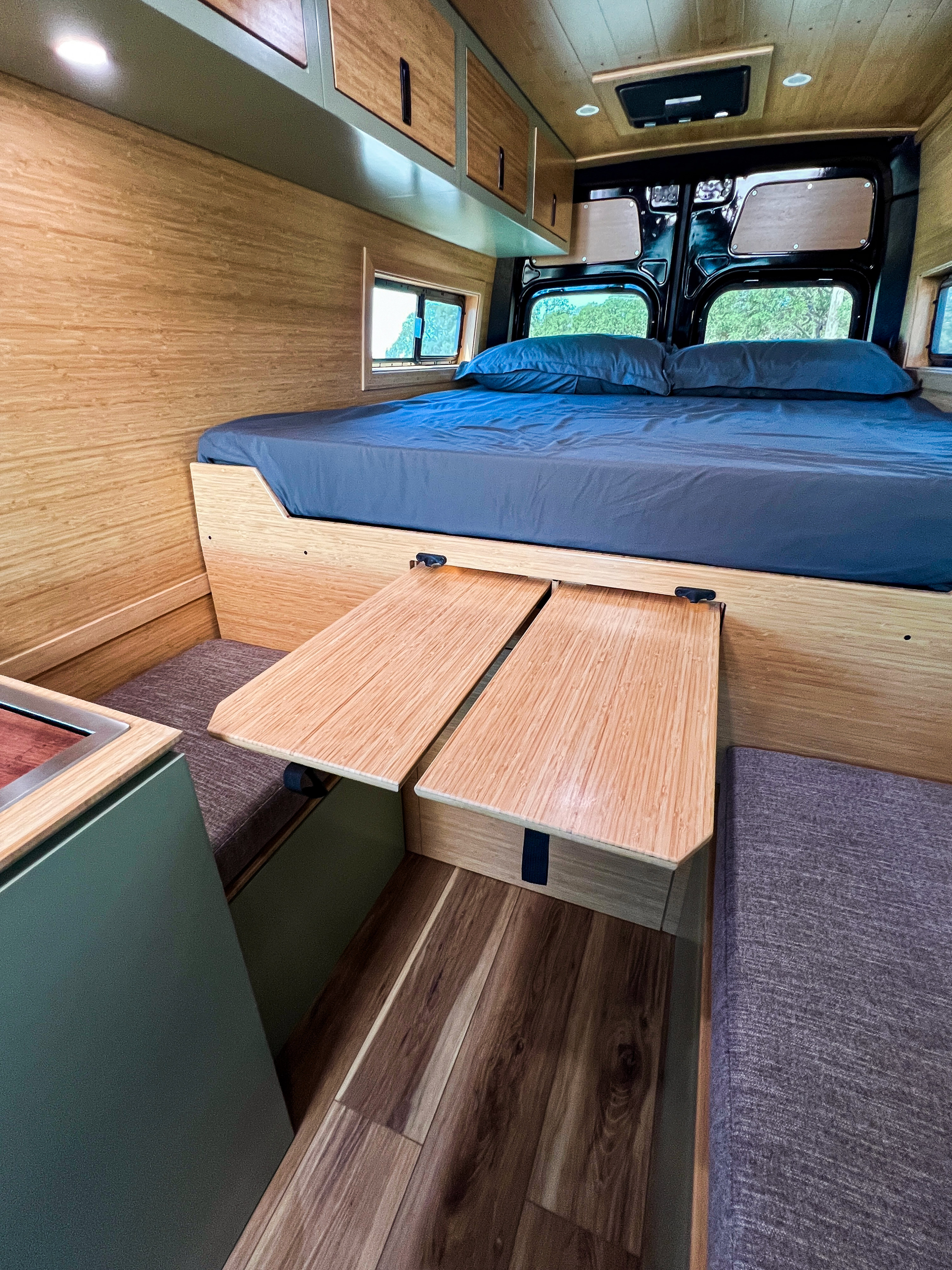 Inside an RV rental camper van: comfortable bed, clever bamboo pull-out tables, and sleek storage solutions with wood finishes.. Mercedes-Benz Sprinter 2500 2024
