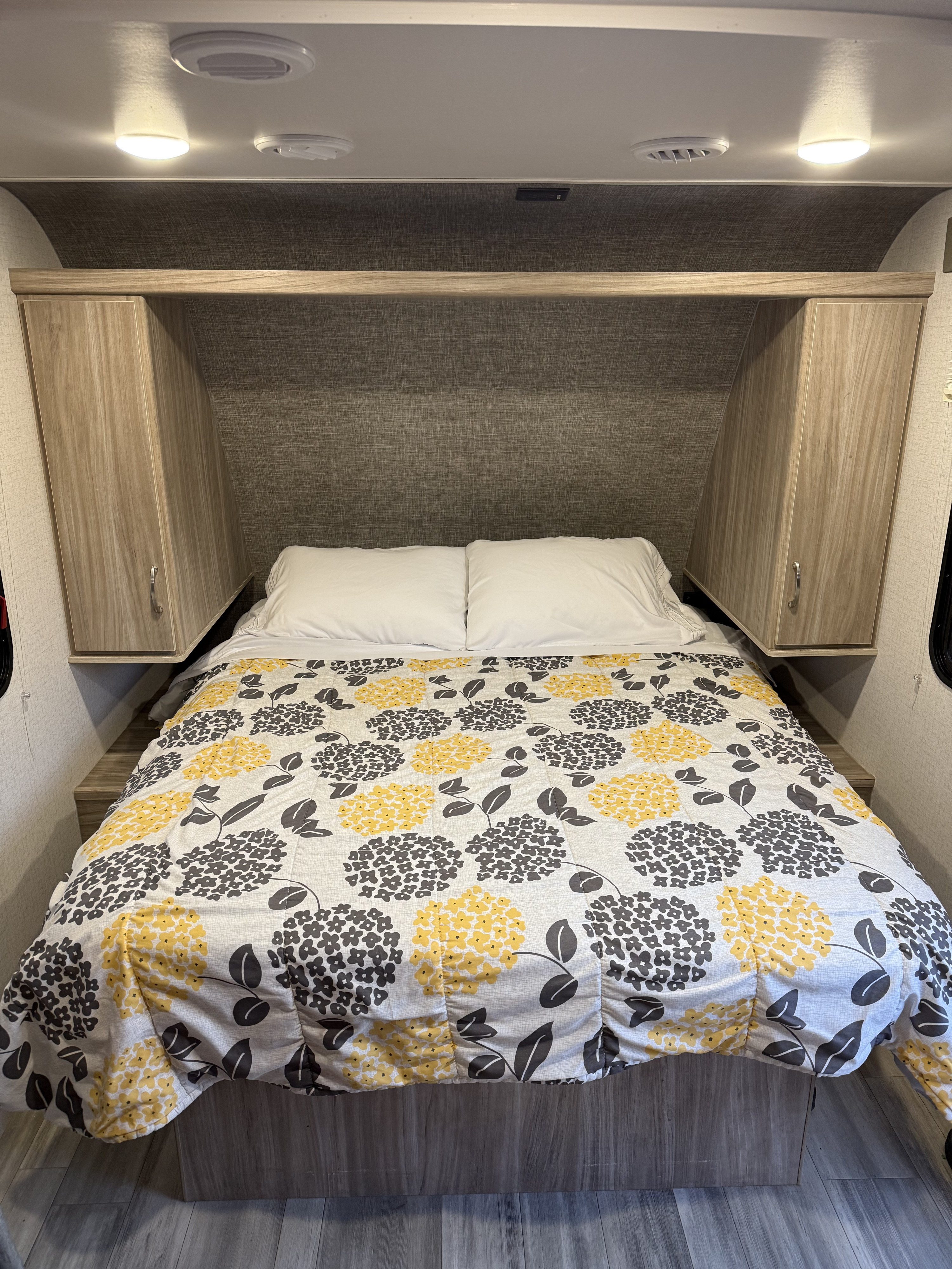 Cozy RV rental bedroom with a floral comforter, white pillows, wood-tone storage, ceiling lights, and vents.. Winnebago 2108FBS 2022