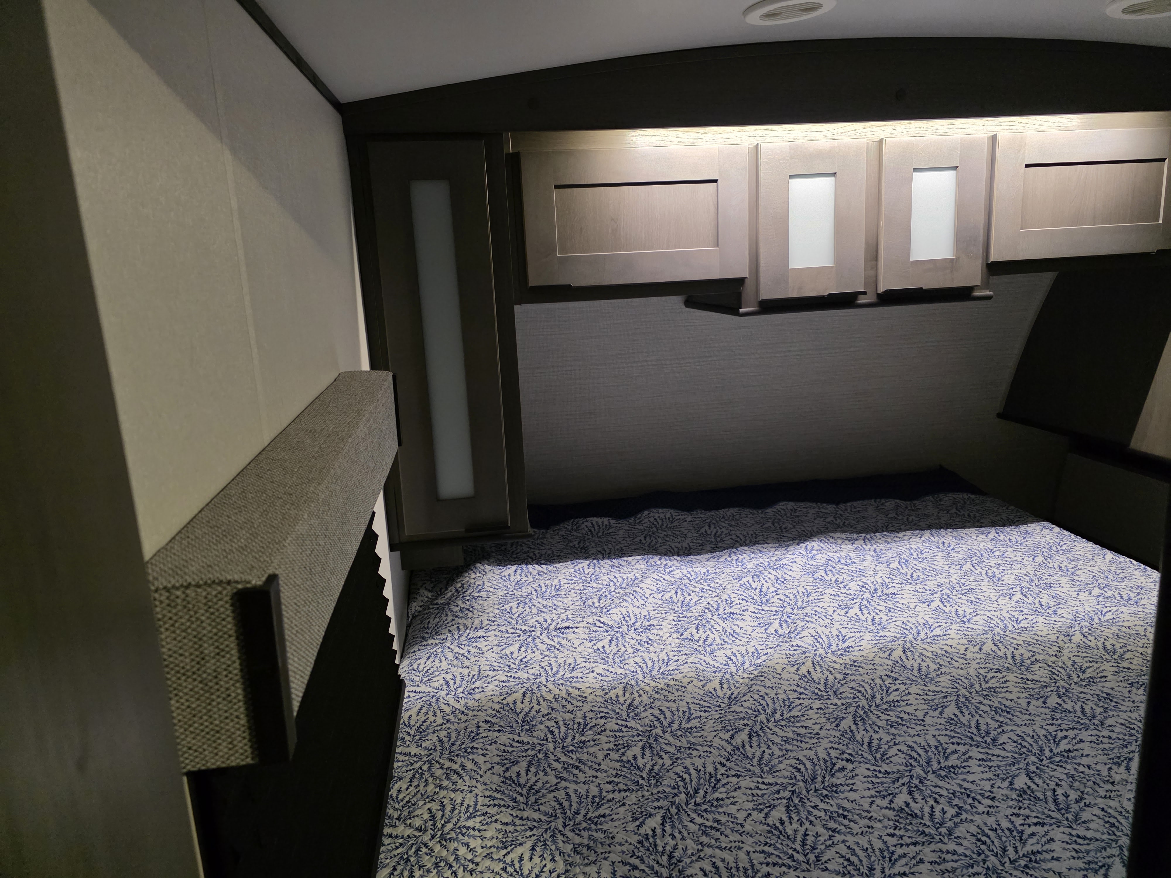 Inside an RV rental, a well-appointed bedroom features a blue patterned bed, overhead cabinets, and soft lighting for travel comfort.. Cruiser RV MPG Ultra Lite 2021