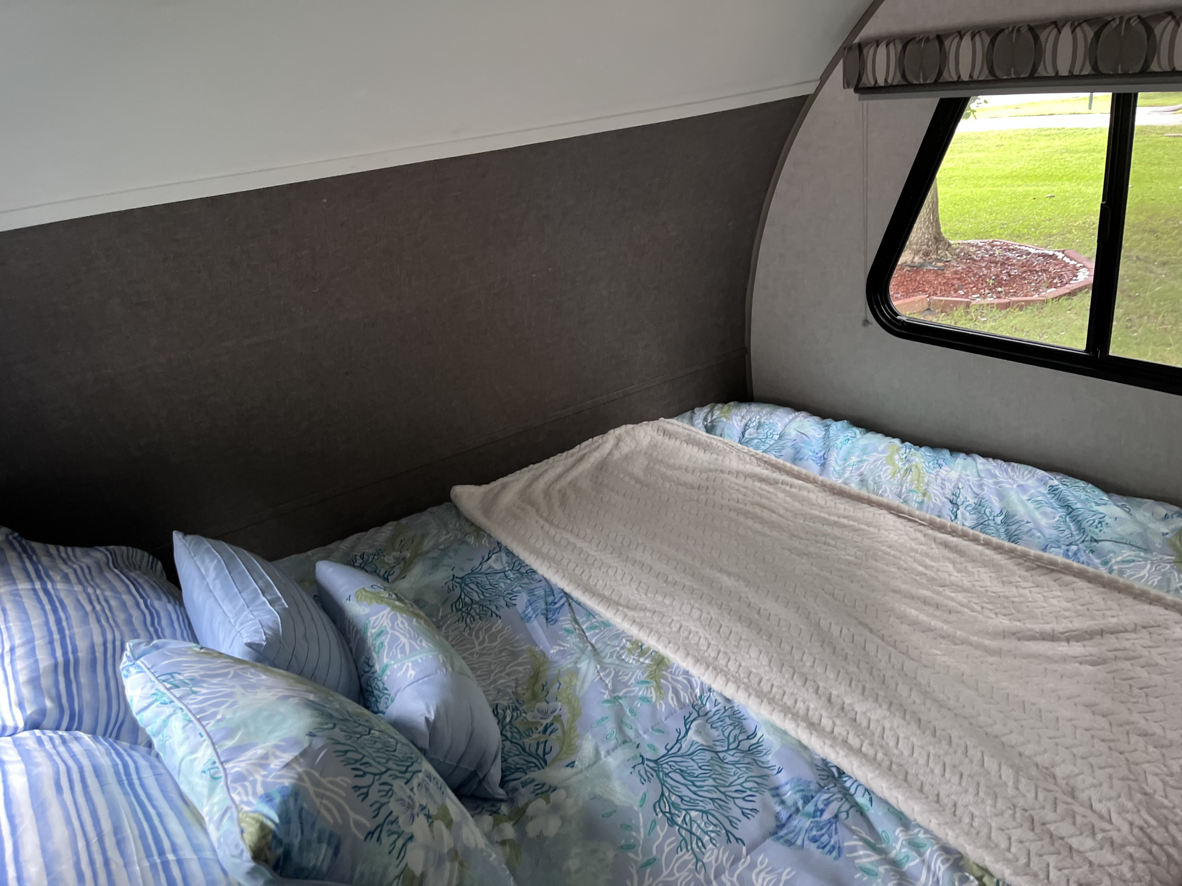 Inside an RV rental, a neatly made bed with blue coastal bedding and a window overlooking a vibrant green outdoor scene.. R-Pod R-Pod Trailer 2018
