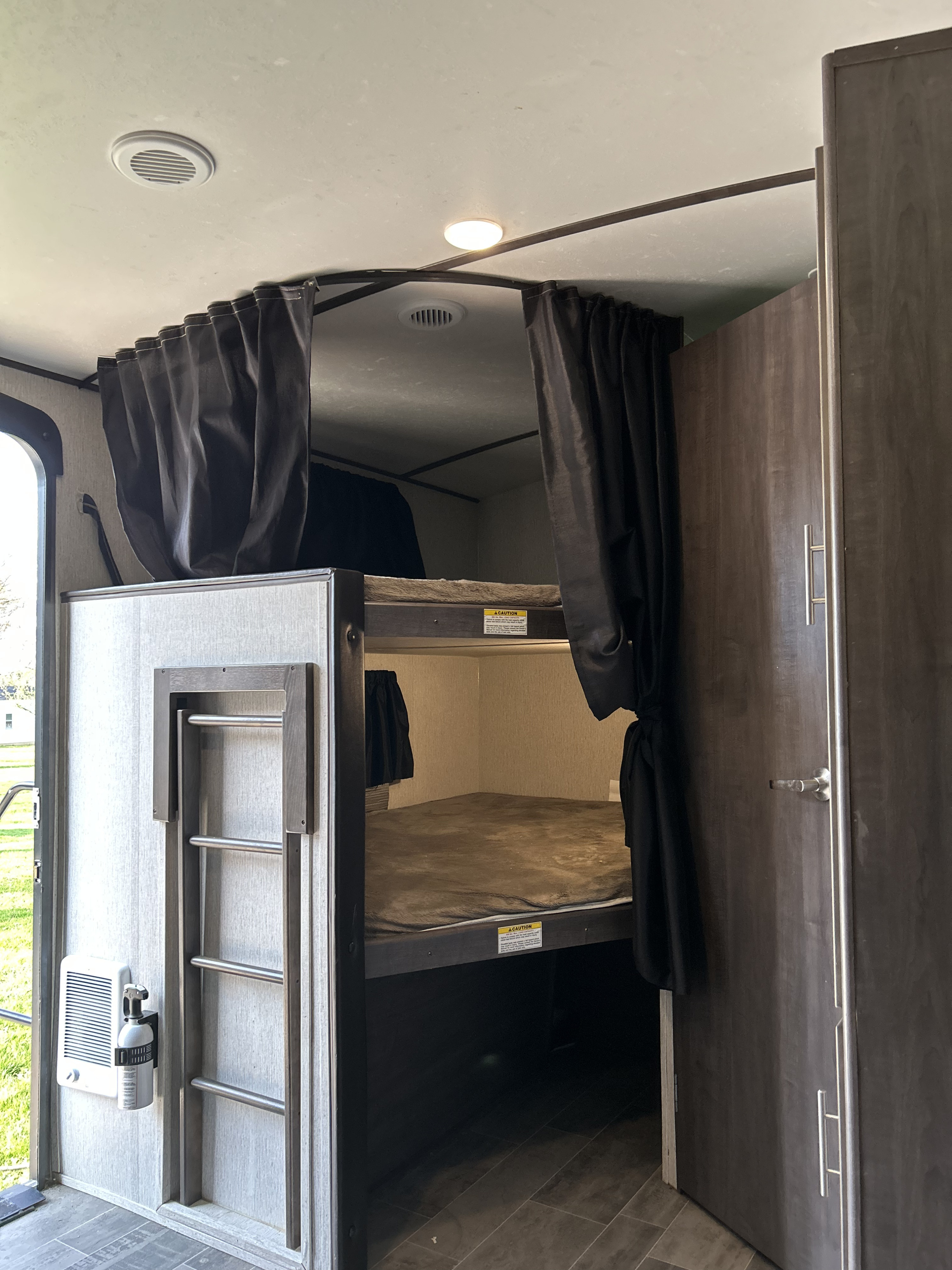 Inside an RV rental, this bunk bed area features privacy curtains, a ladder for the top bunk, and adjacent storage.. Crossroads RV Sunset Trail Super Lite 2019