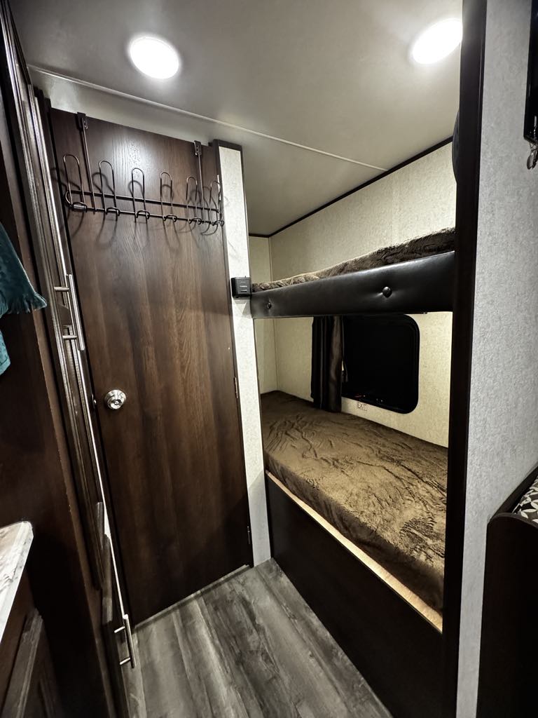 Cozy RV rental interior featuring comfortable bunk beds, a dark wood door with an organizer, and wood-look flooring.. Jayco Jay Flight SLX 2019