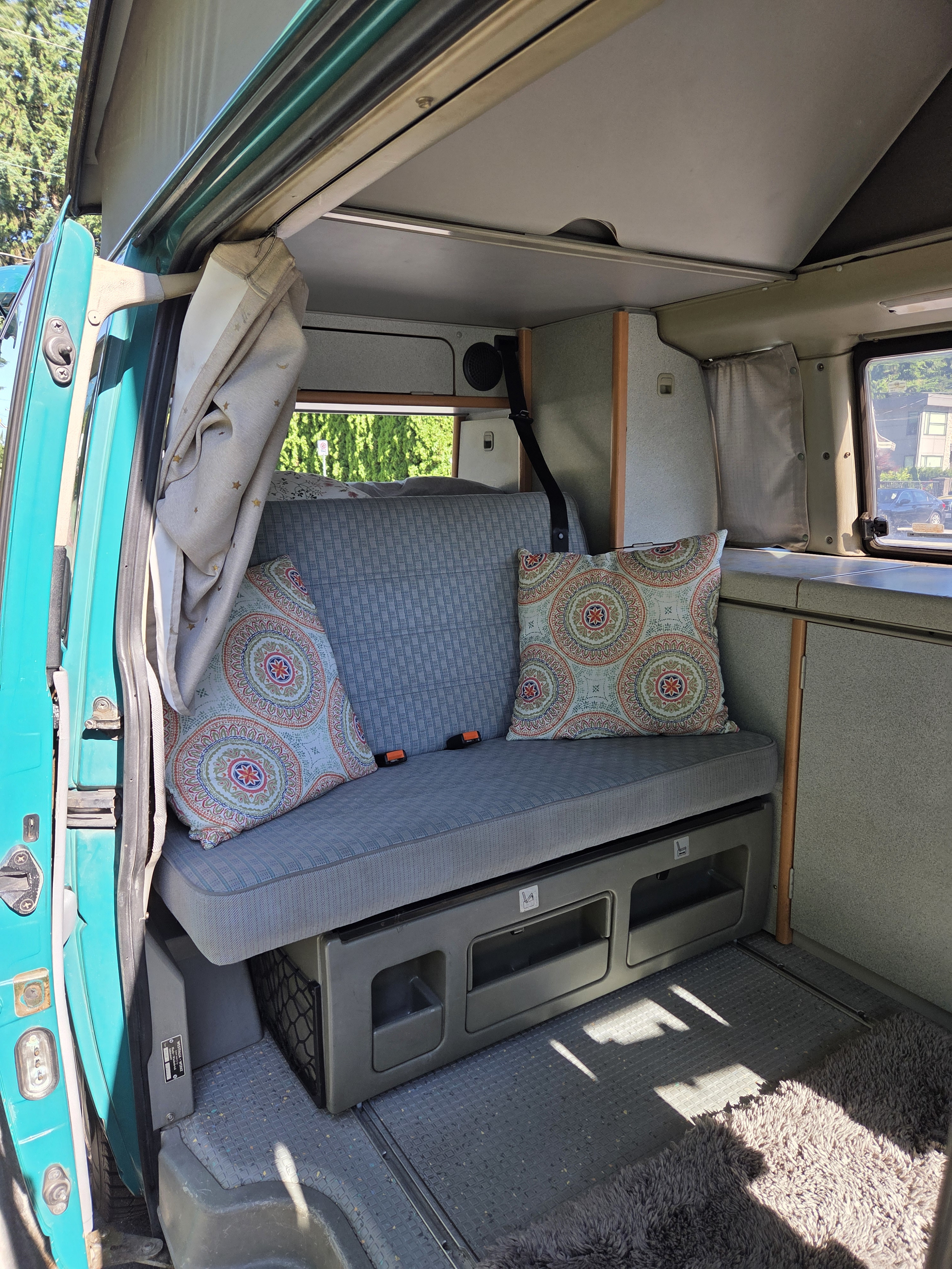 Inside this RV rental, a comfy bench seat with vibrant pillows, storage, and a pop-top roof create a functional living space.. Westfalia T4 California Coach 1998