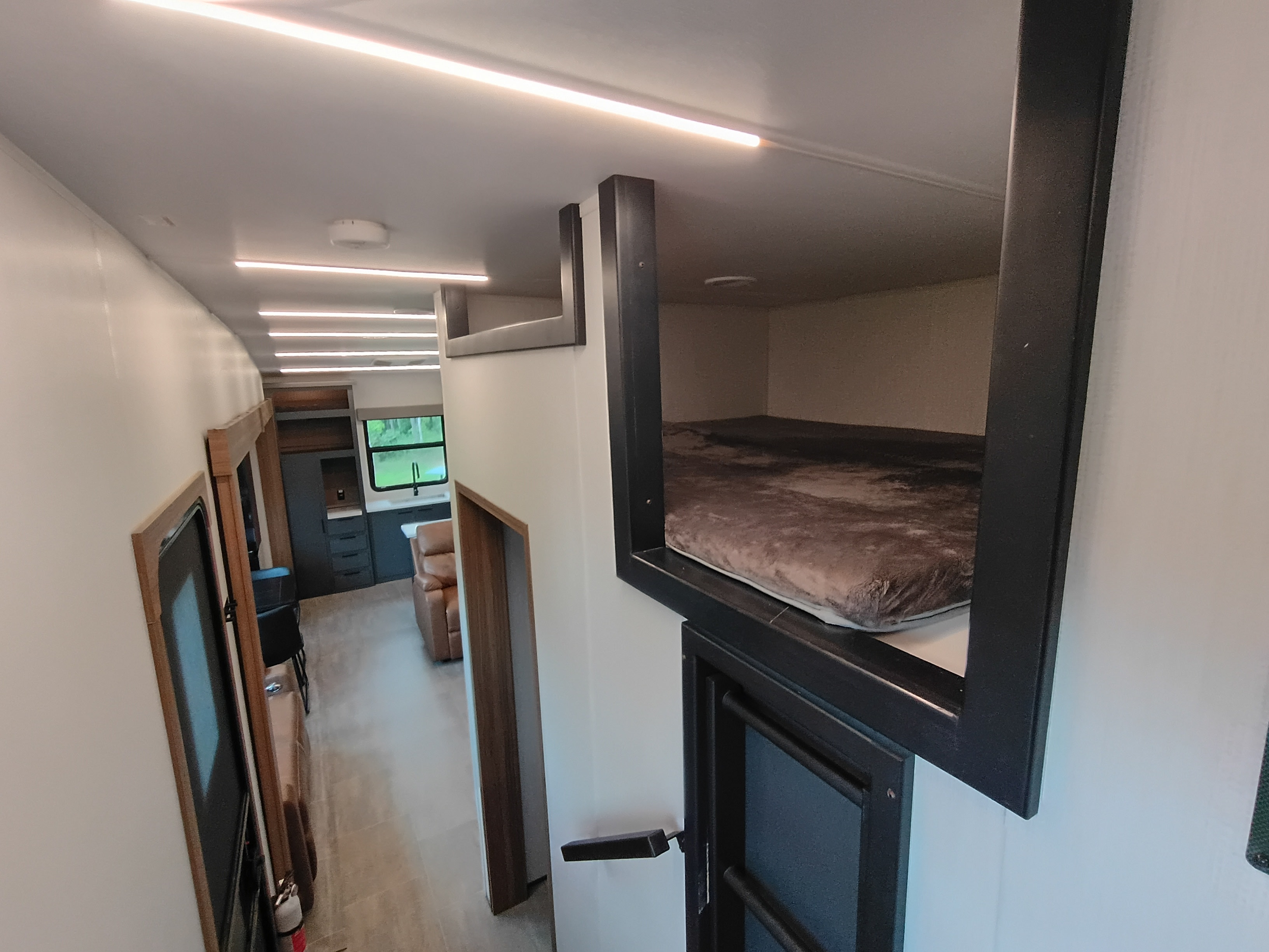 Modern RV rental interior: overhead bunk bed, compact living space with kitchen & window view.. Heartland Corterra 2025