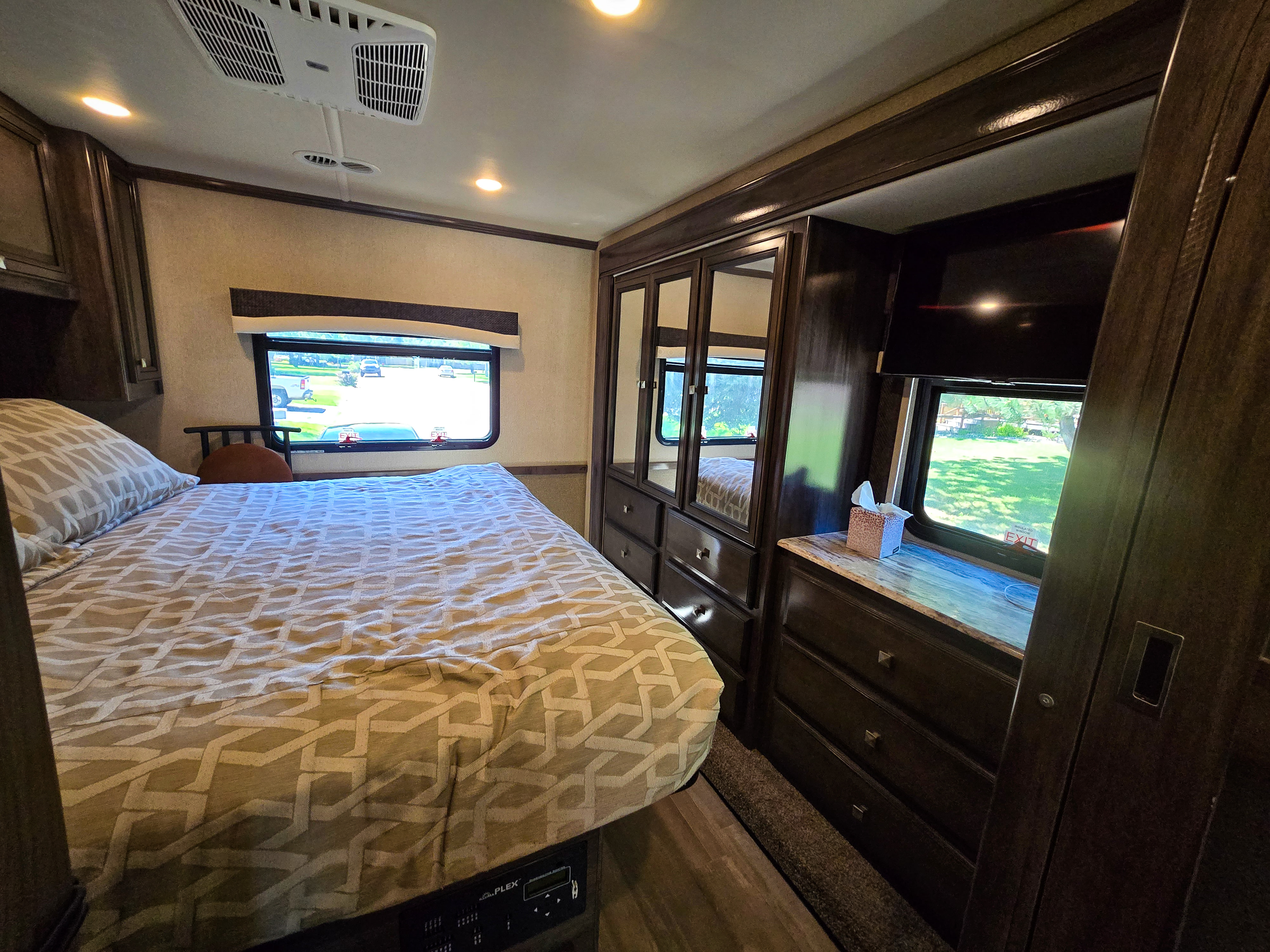 Spacious RV bedroom with comfortable bed, mirrored closets, TV, and outdoor views, perfect for an RV rental.. Flair-Fleetwood Flair-Fleetwood Motorhome 2019