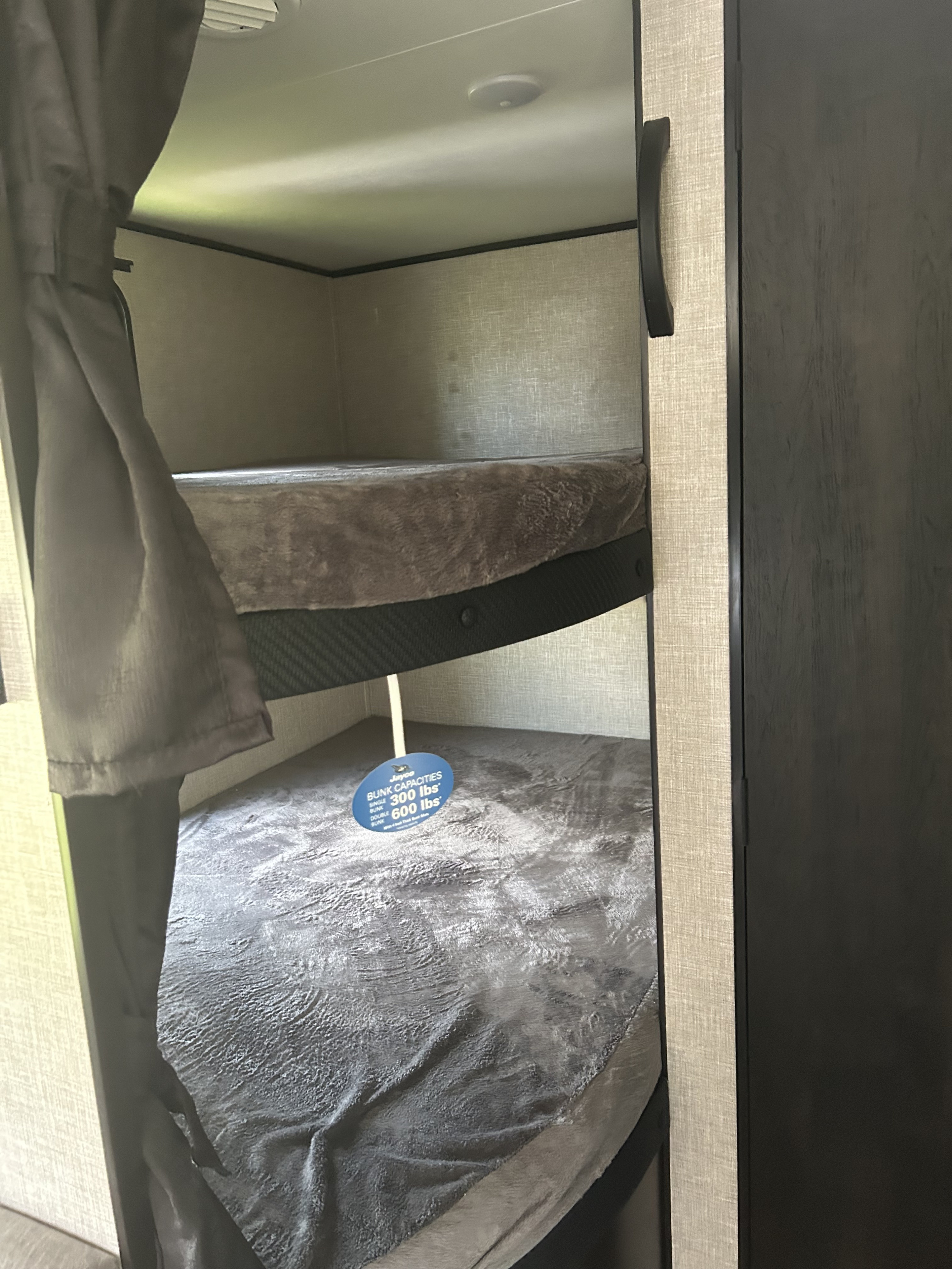 RV rental interior: two bunk beds with gray bedding. A sign indicates single bunk capacity 300 lbs, double 600 lbs.. Jayco Jay Flight 2023