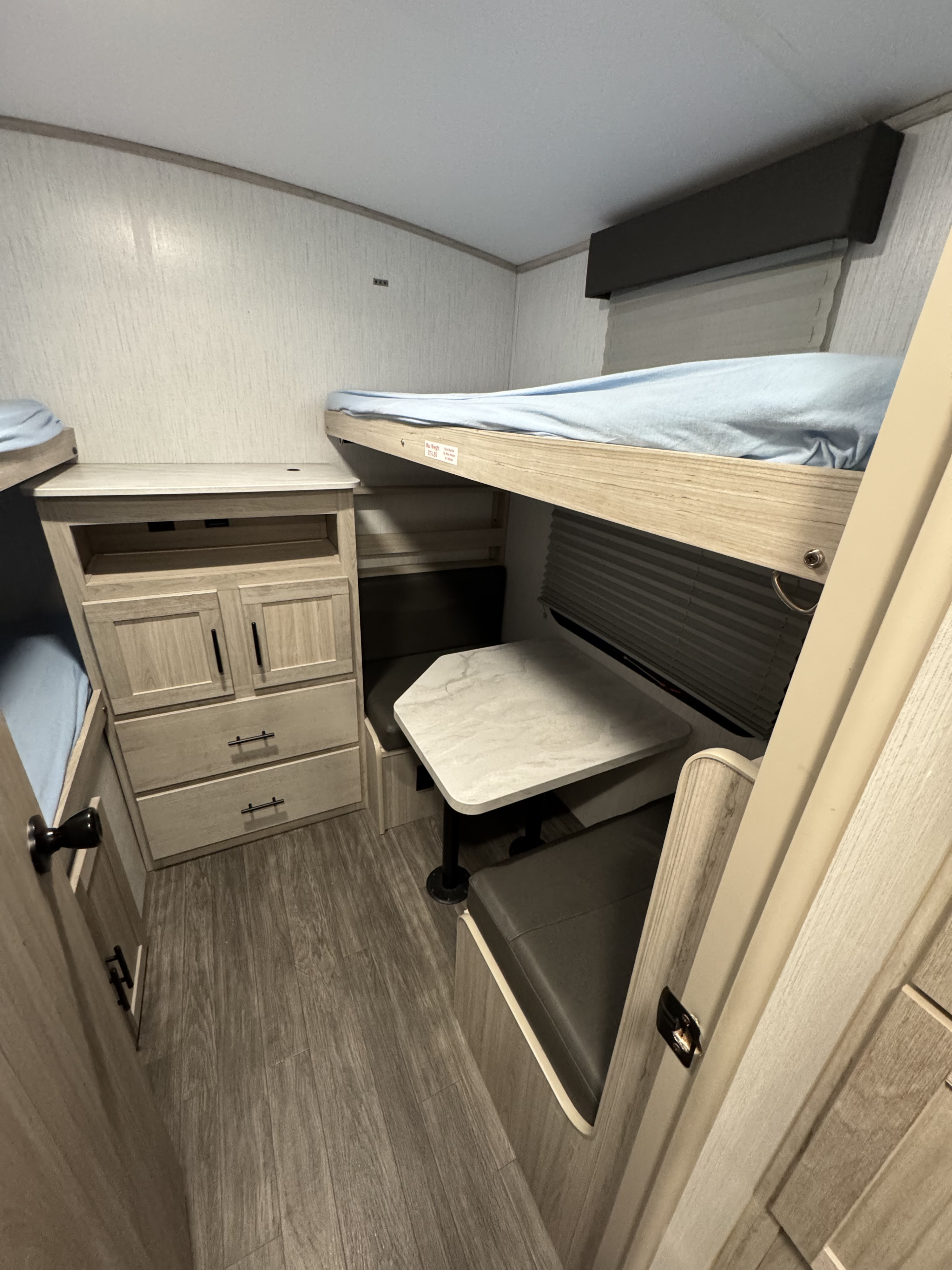 Interior of an RV rental: light wood-paneled bunk beds, dinette table, and storage cabinets on wood-look flooring.. Cruiser RV Shadow Cruiser 2022