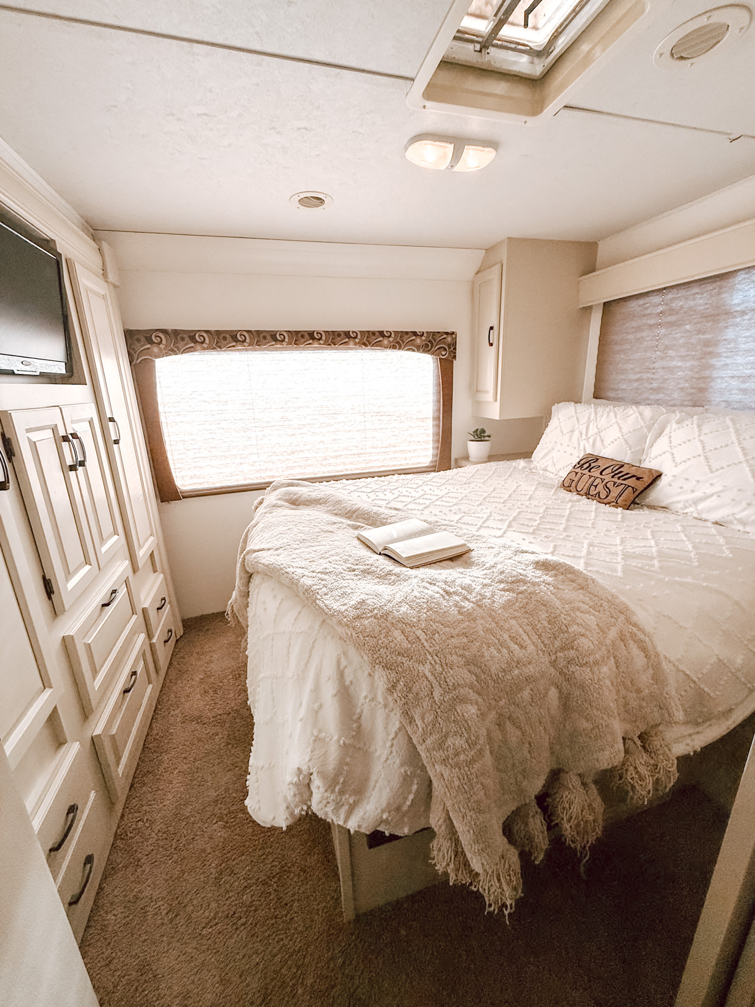 Cozy RV rental bedroom with white bedding, "Be Our Guest" pillow, TV, and ample storage for travel.. Forest River Sunseeker 2015