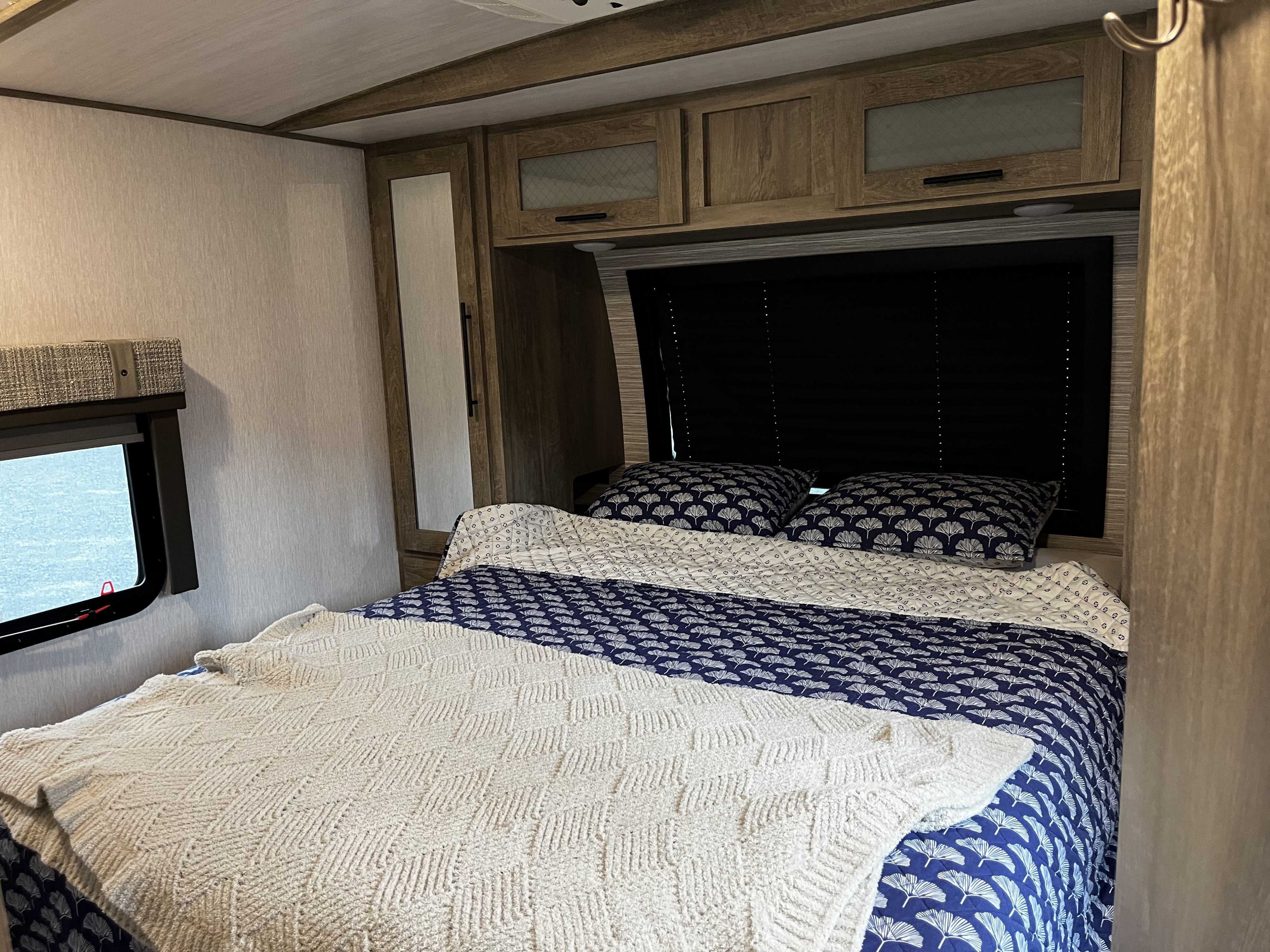 Cozy RV rental bedroom features a bed with blue patterned bedding, a textured white blanket, and wood cabinets.. Forest River Salem Hemisphere 2022