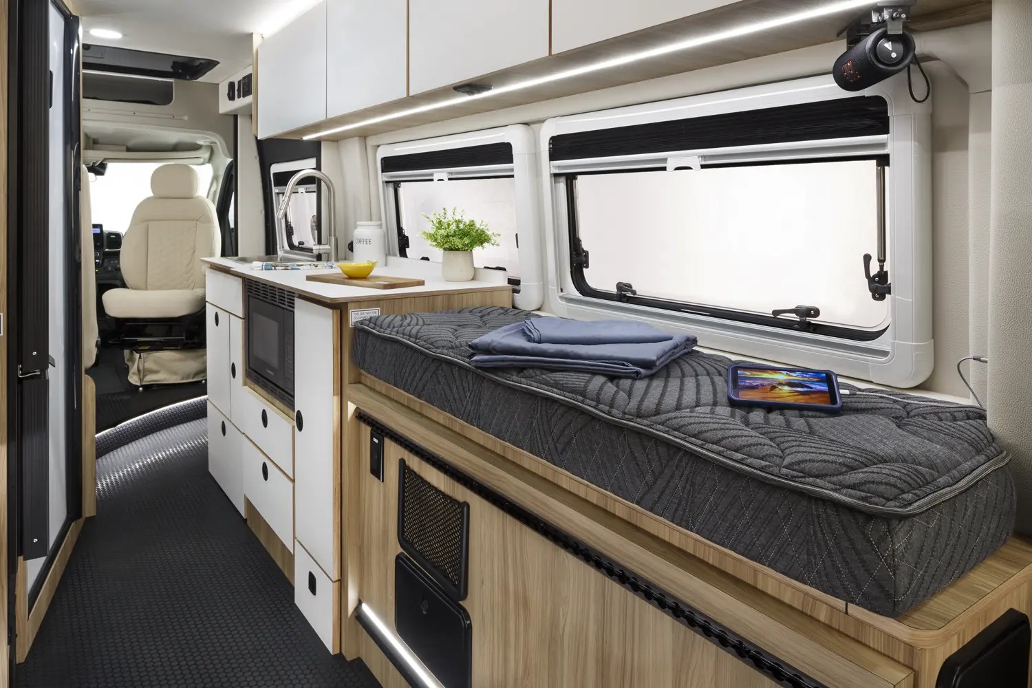 Modern rv rental interior: compact kitchen (sink, microwave), comfortable bed, and storage. Ideal for camper van travel.. Coachmen PIXEL 2026