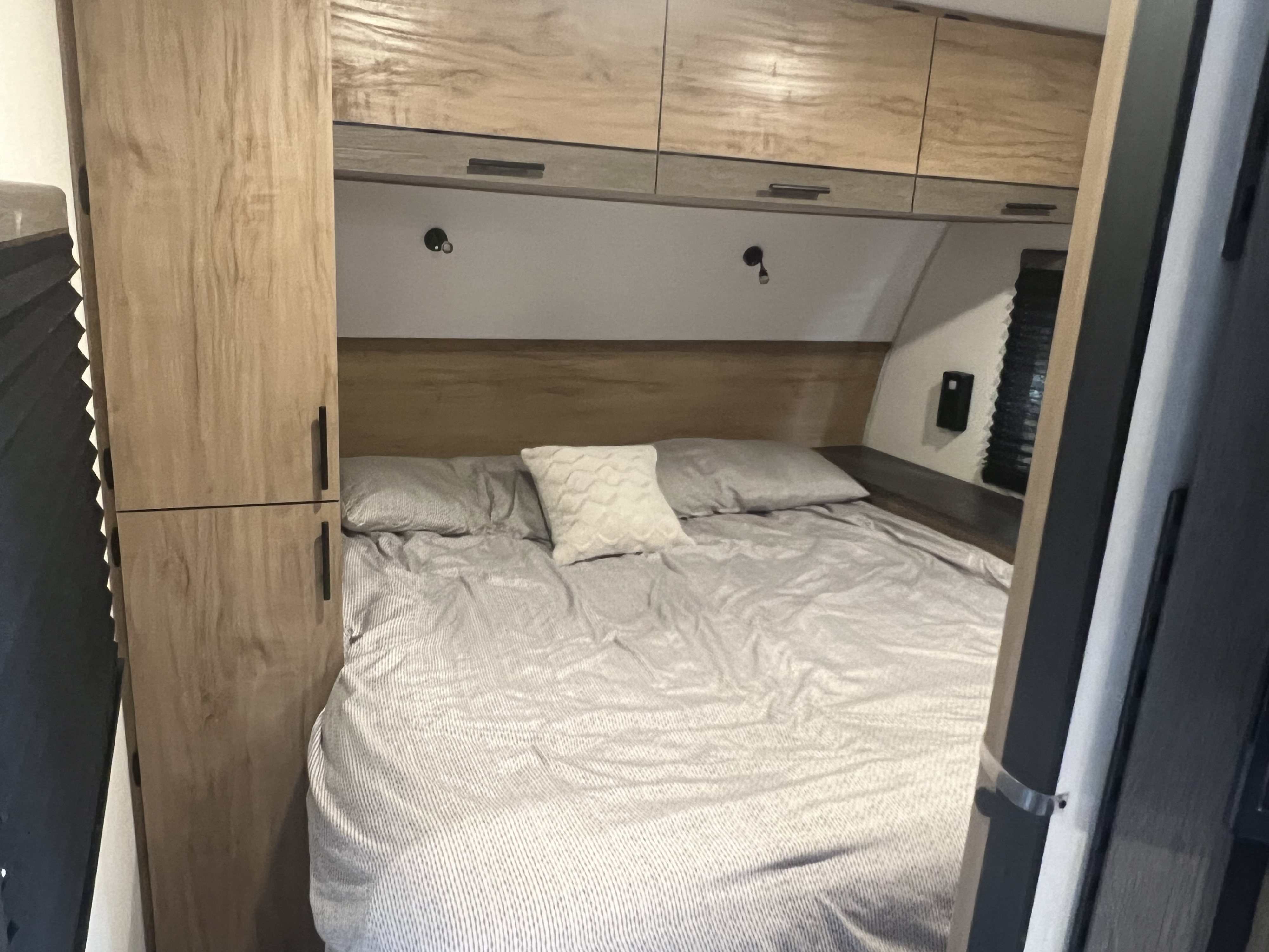 Cozy RV rental bedroom with striped bedding, overhead storage, and reading lights, offering a comfortable sleeping area.. Forest River Campsite reserve 25MW 2025