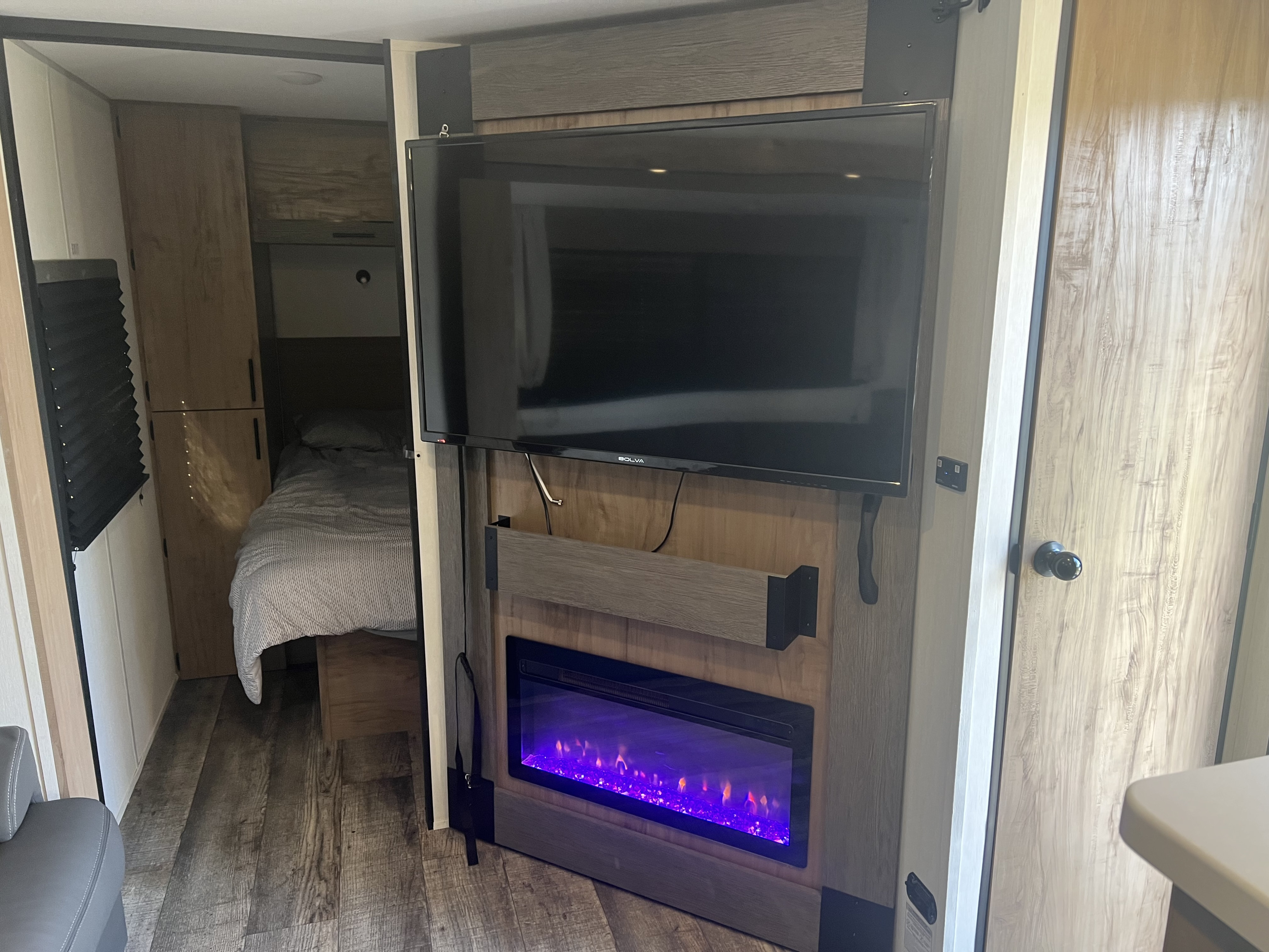 Cozy RV rental interior with a flat-screen TV, glowing purple electric fireplace, and adjacent bedroom.. Forest River Campsite reserve 25MW 2025