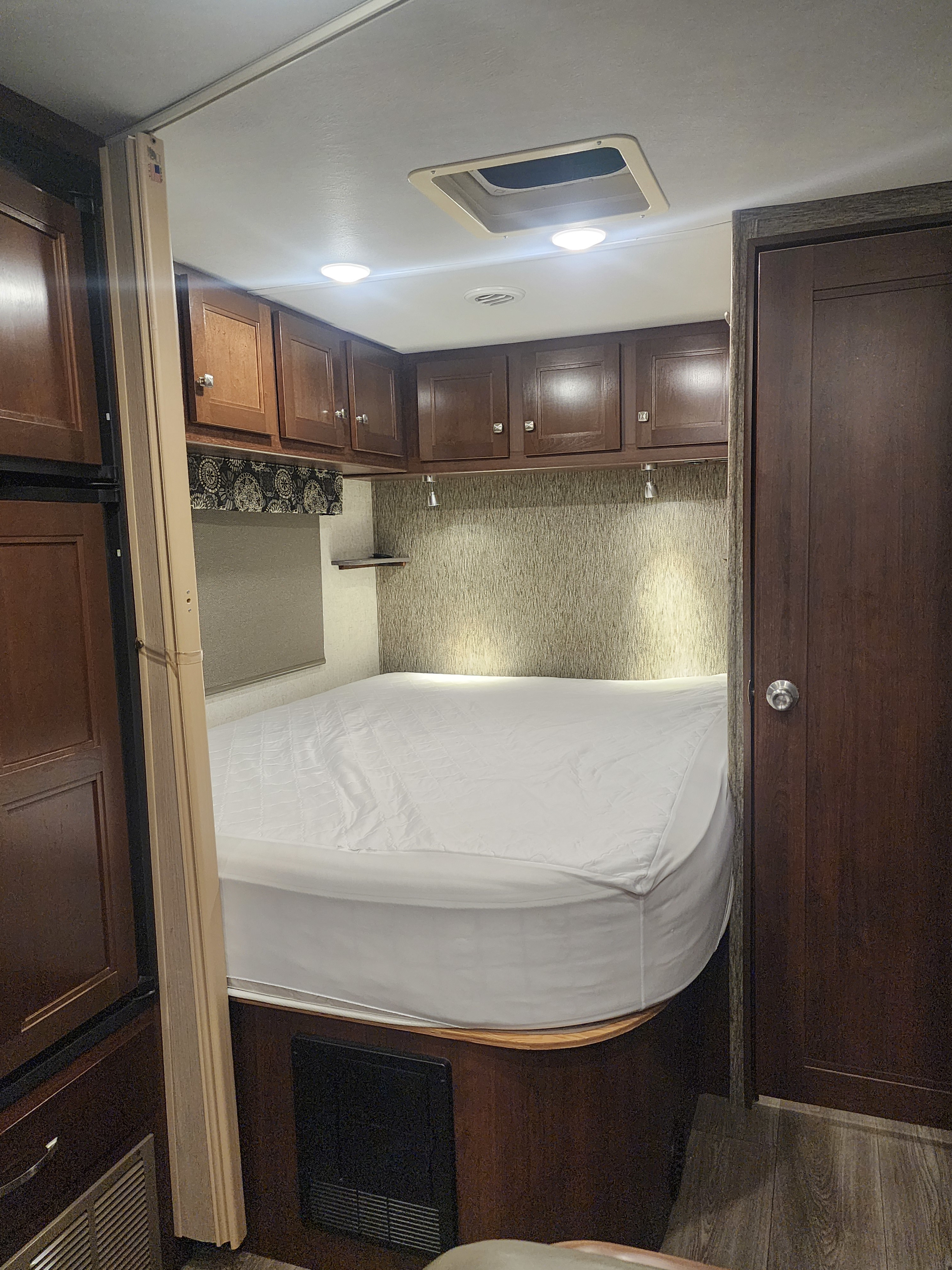 Cozy RV rental bedroom featuring a white bed, dark wood cabinets, and warm lighting, ready for your travels.. Forest River Forester 2018