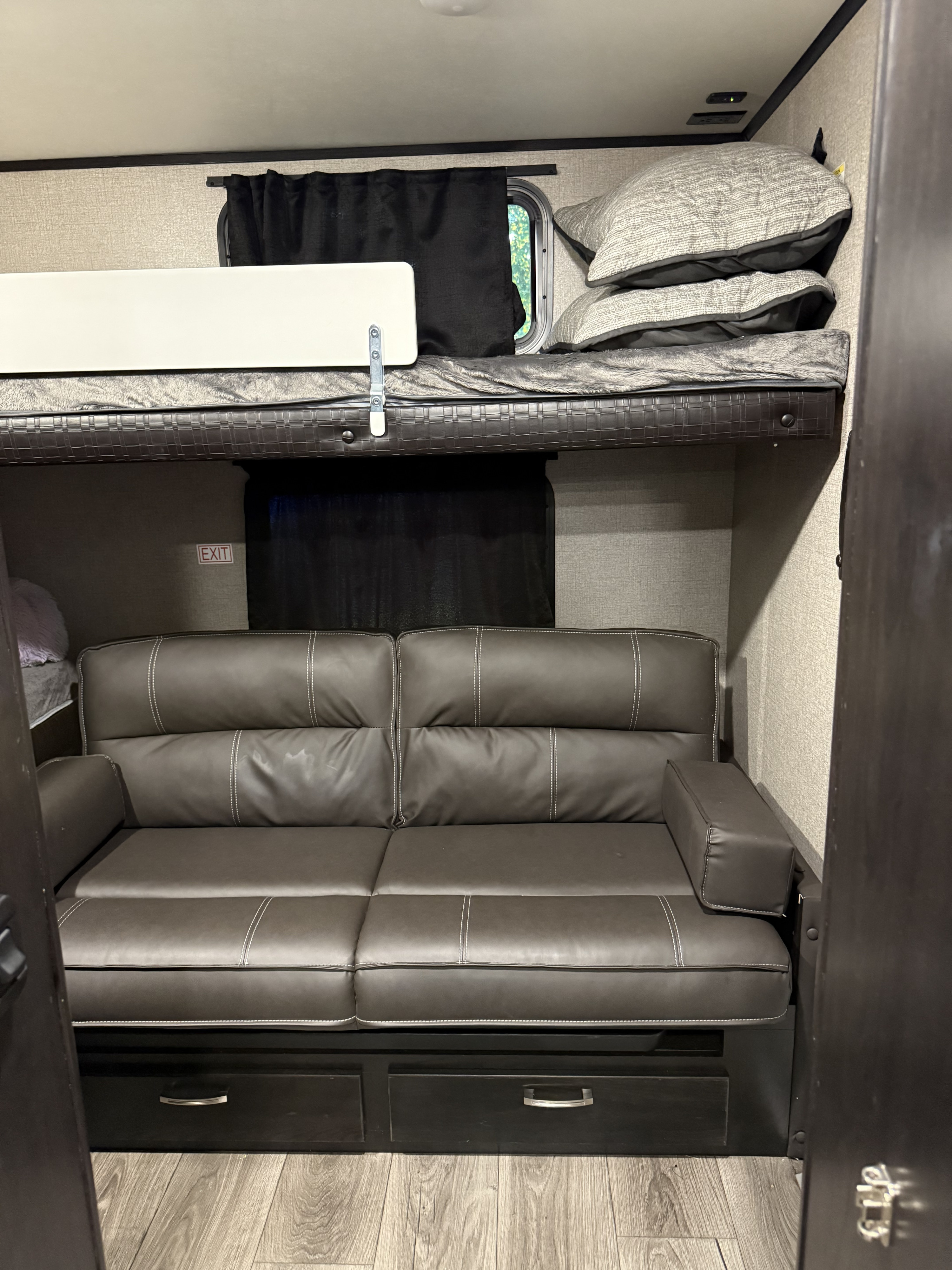 Inside a cozy RV rental: Features a comfortable bunk bed above a gray leather sofa with integrated storage.. Jayco Jay Feather 2021