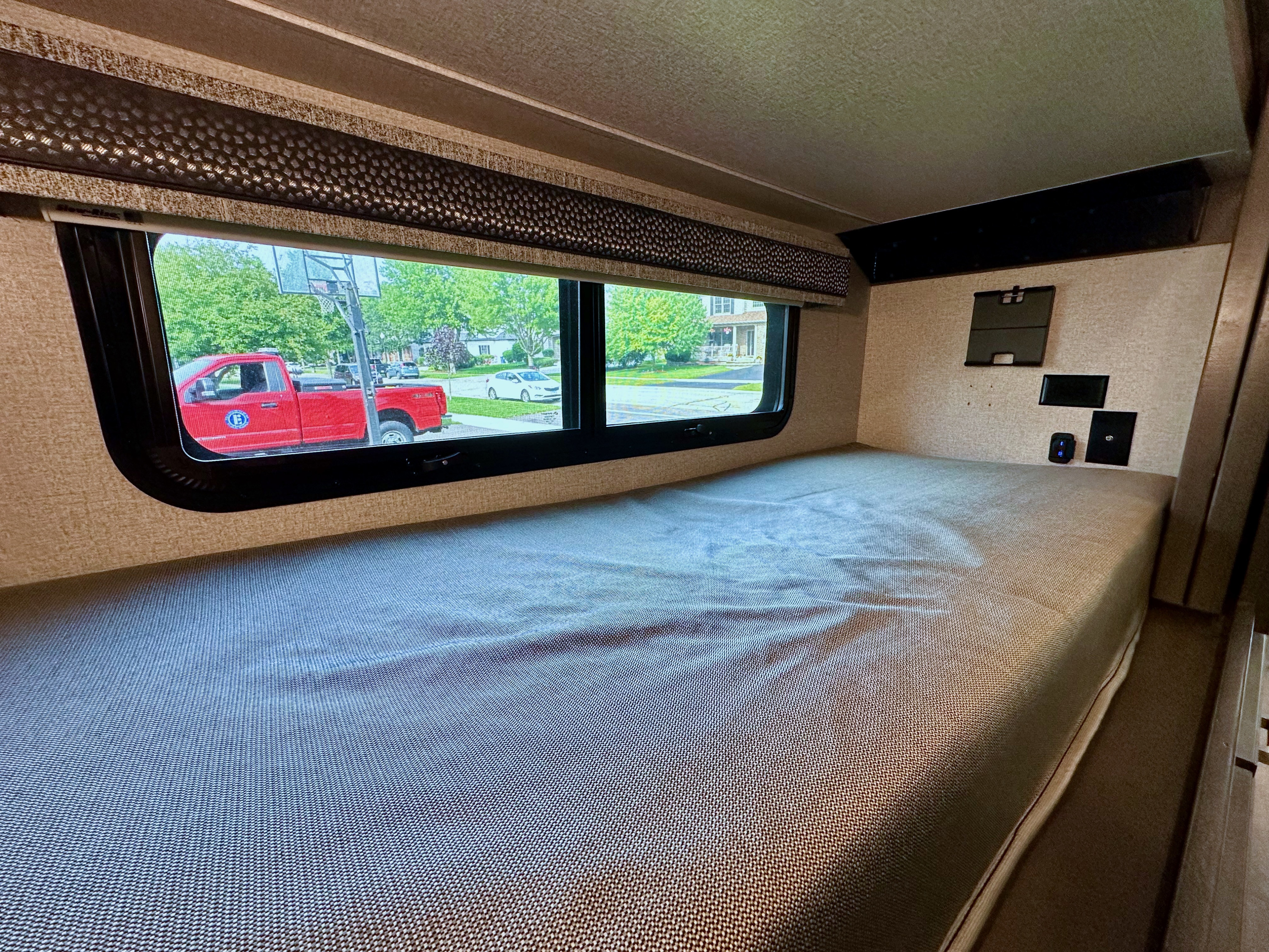 Cozy RV rental bunk bed with a window view of a residential street. Perfect for a comfortable stay.. Thor Luminate 2023