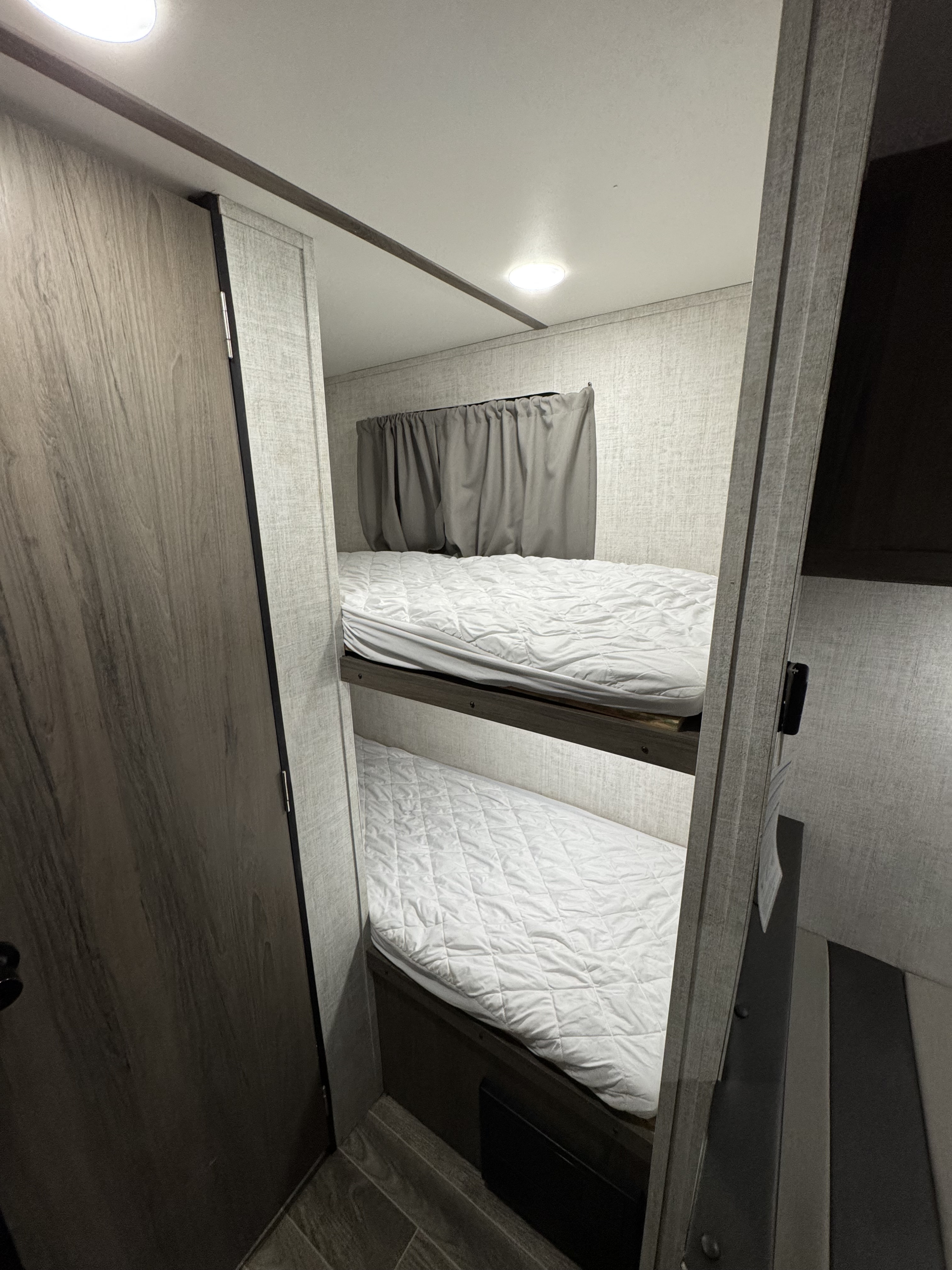 This RV rental features two clean bunk beds with white quilted mattresses, a window with grey curtains, and light-colored walls.. Gulf Stream Ameri-Lite Super Lite 2022