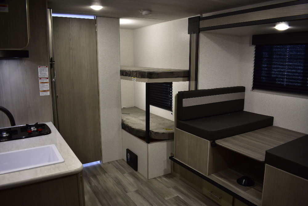 This RV rental's interior features a kitchen sink & stove, two bunk beds, and a dinette next to a window.. Keystone RV Springdale 2024