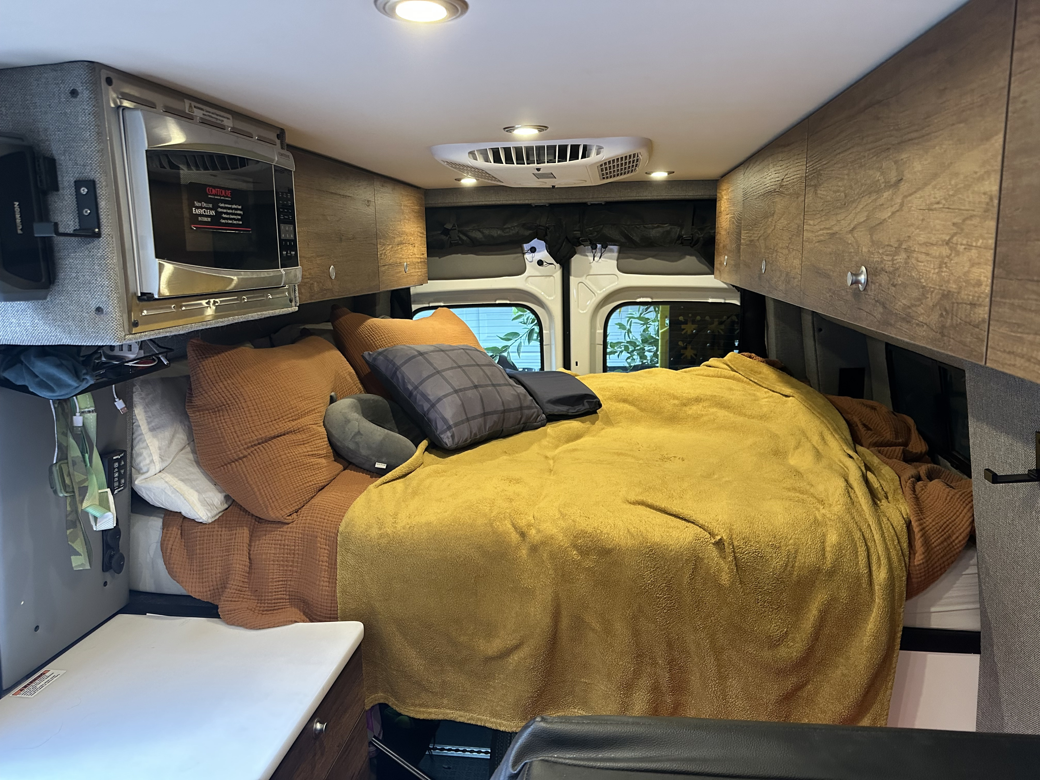 Cozy RV rental interior features a comfortable bed, microwave, and overhead cabinets.. Storyteller Overland Storyteller Overland Class B 2021