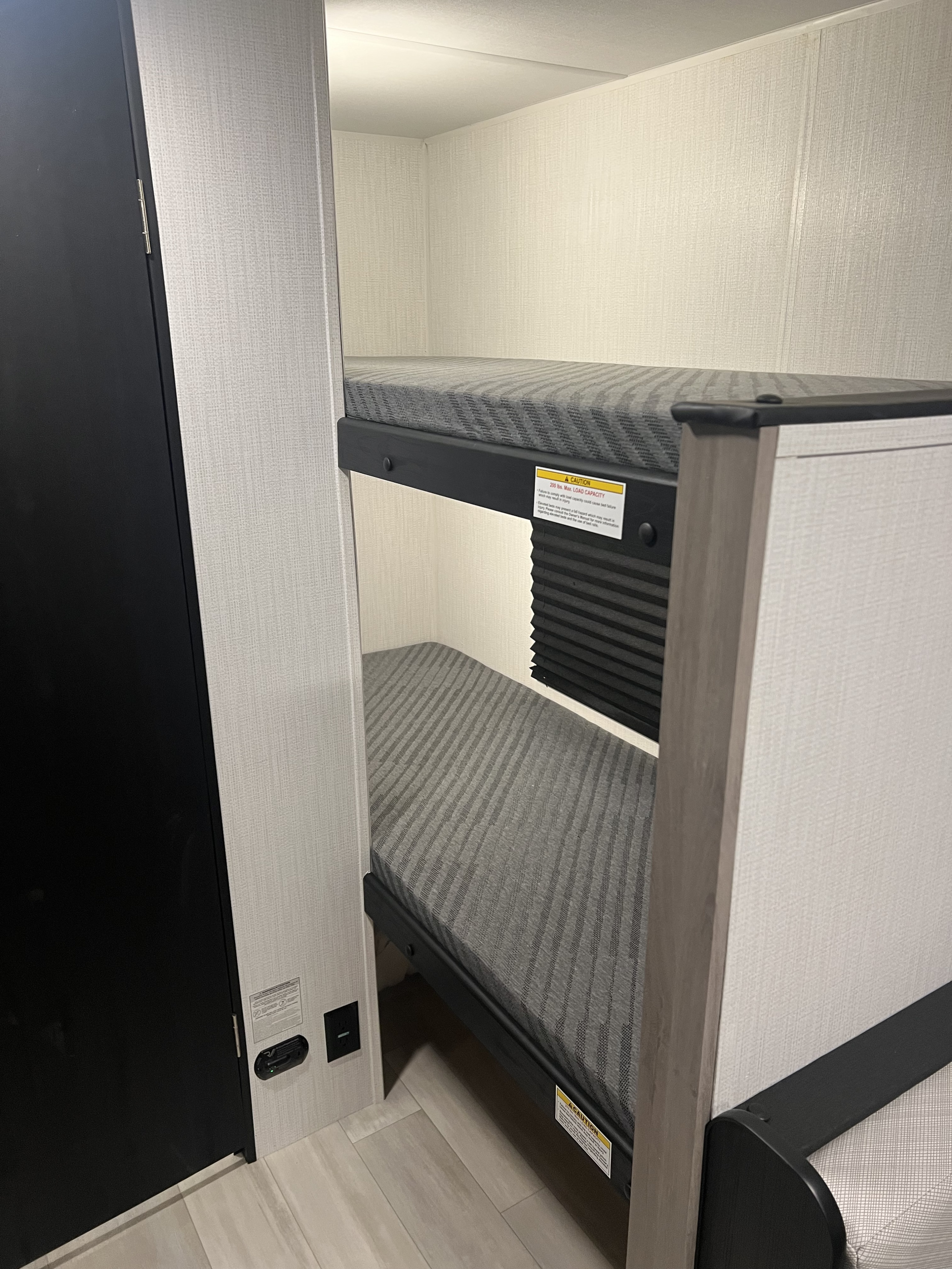 A cozy RV rental interior features compact bunk beds with chevron-patterned mattresses and safety warnings.. Heartland Prowler Lynx 17BHX 2025