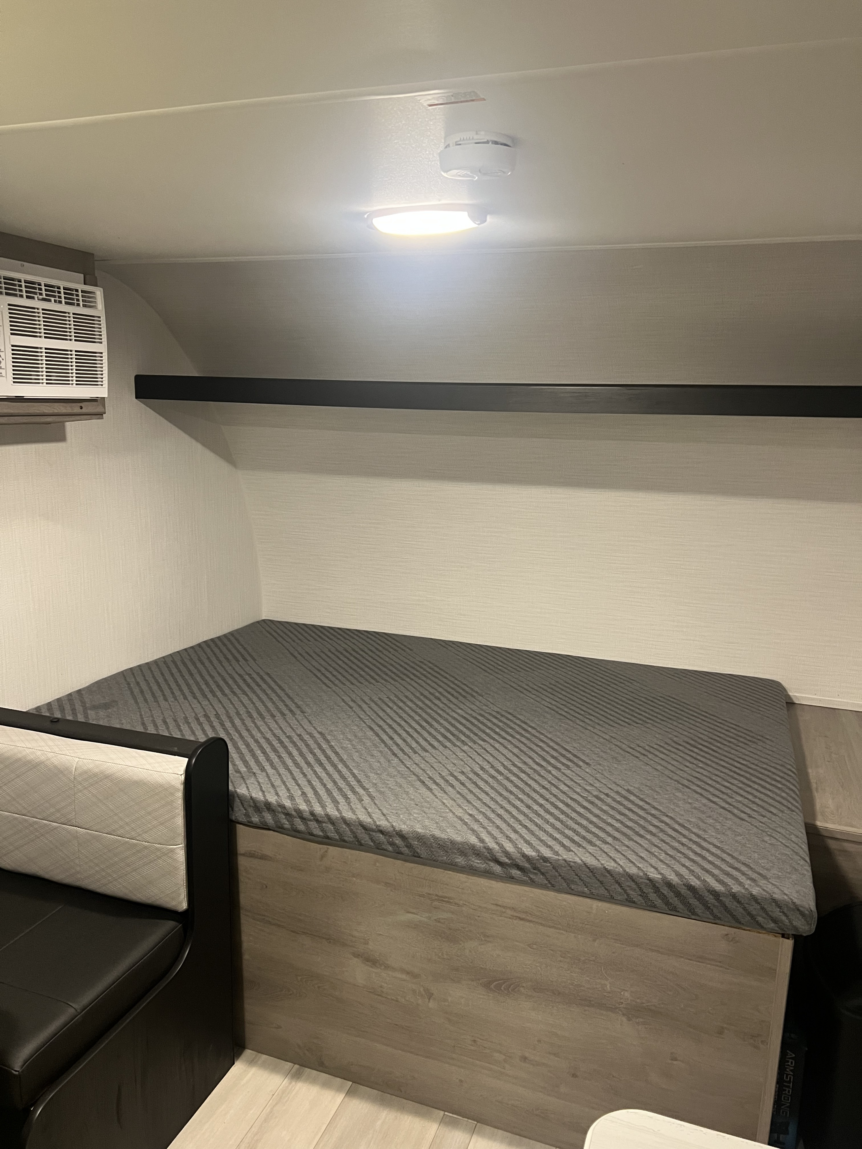 RV rental bedroom featuring a gray striped mattress, black floating shelf, and AC unit inside.. Heartland Prowler Lynx 17BHX 2025
