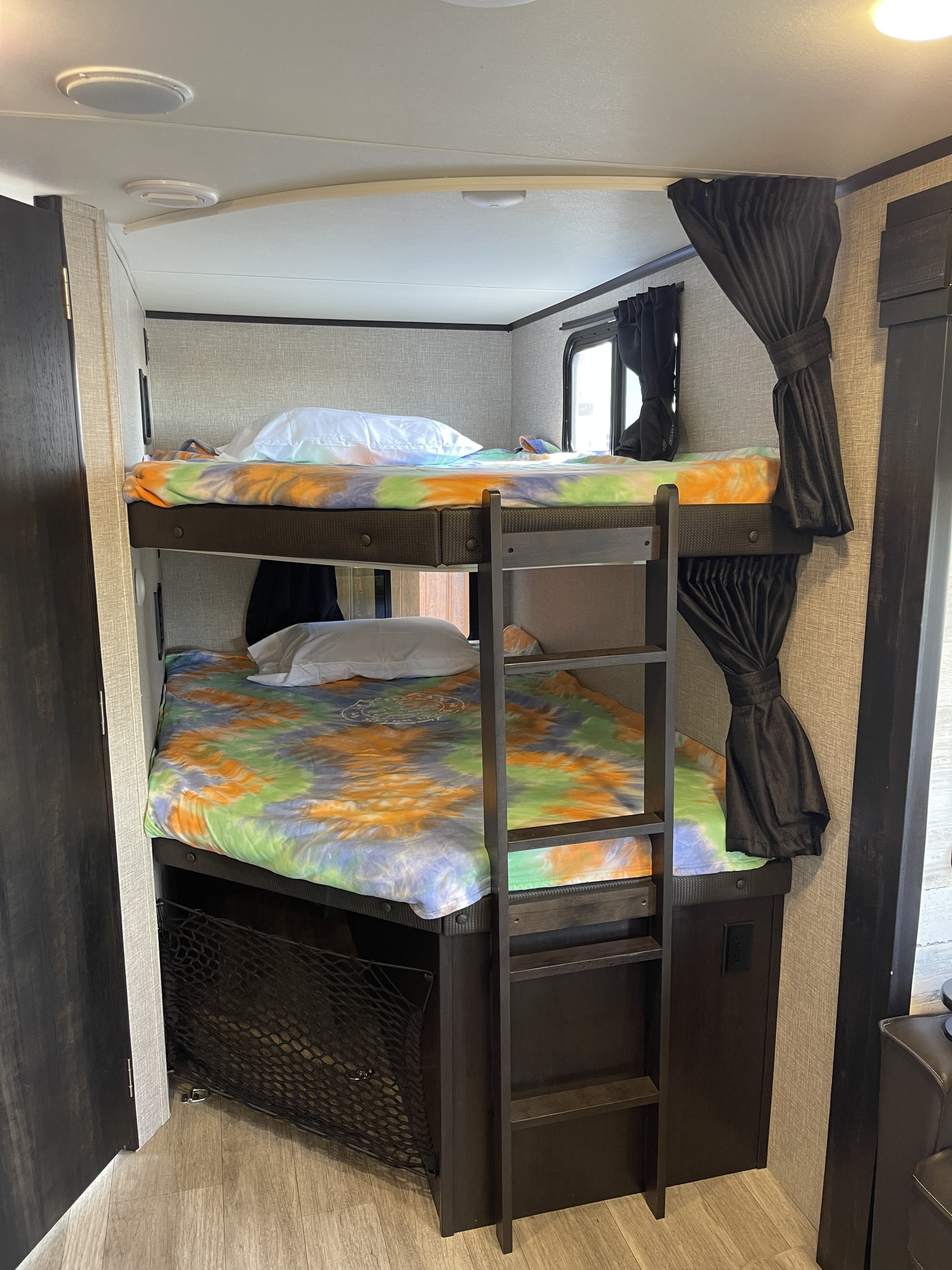 Colorful bunk beds in an RV rental, offering cozy sleeping space with tie-dye bedding, ladder, & storage net.. Jayco Jay Feather 2022