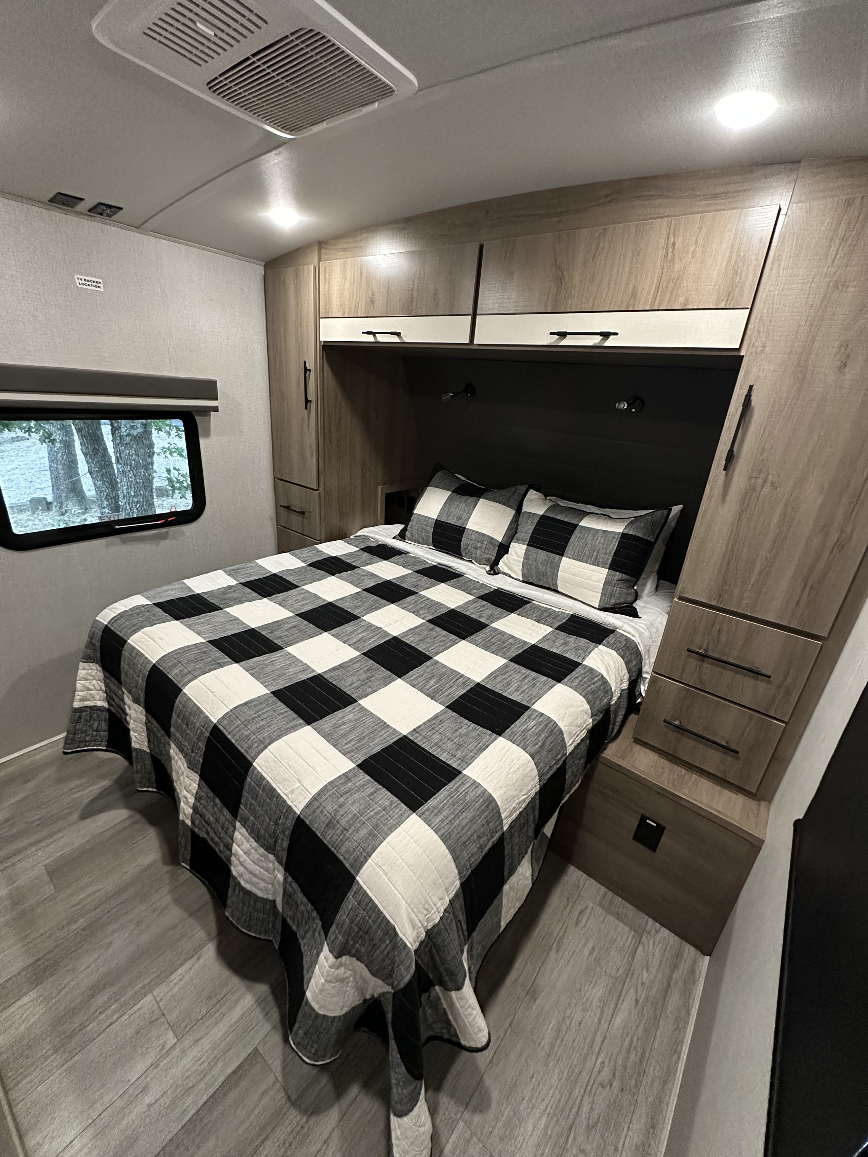 Spacious RV rental bedroom with a comfy black and white plaid bed, ample built-in storage, and an outdoor view. Enjoy your trip!. Grand Design Imagine 2023