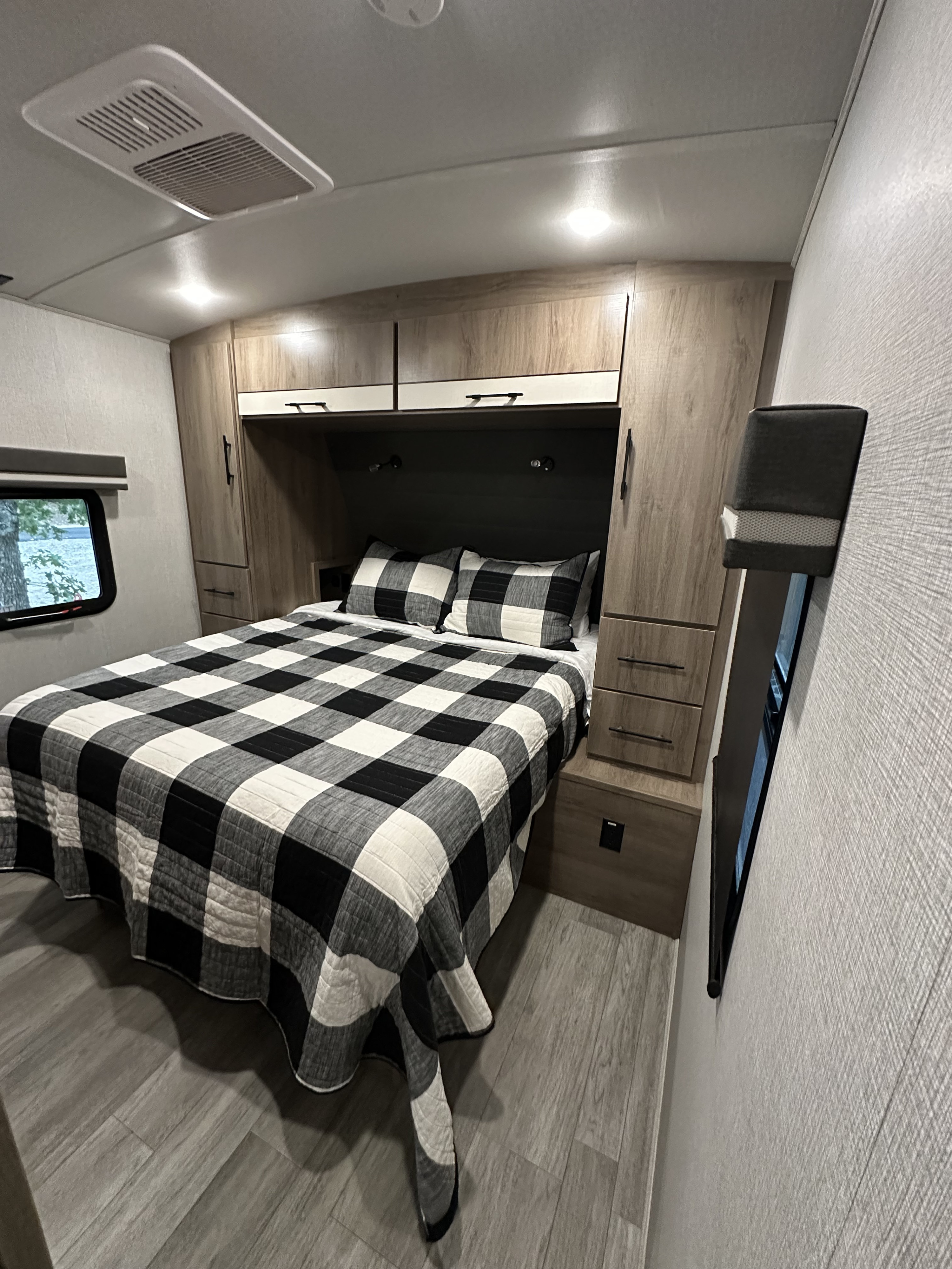 Cozy RV rental bedroom with checkered bedding, built-in storage, and a window view. Perfect for travel!. Grand Design Imagine 2023