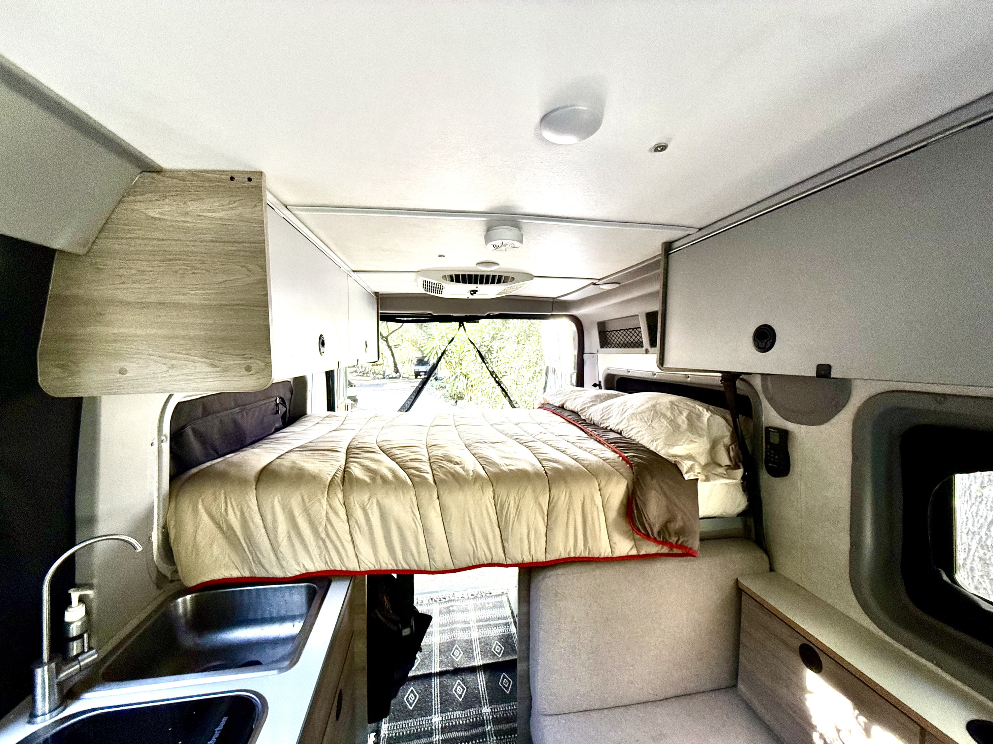 Cozy rv rental interior featuring a comfortable bed, kitchenette, and overhead storage. Ideal camper van living space.. Winnebago Solis 2023